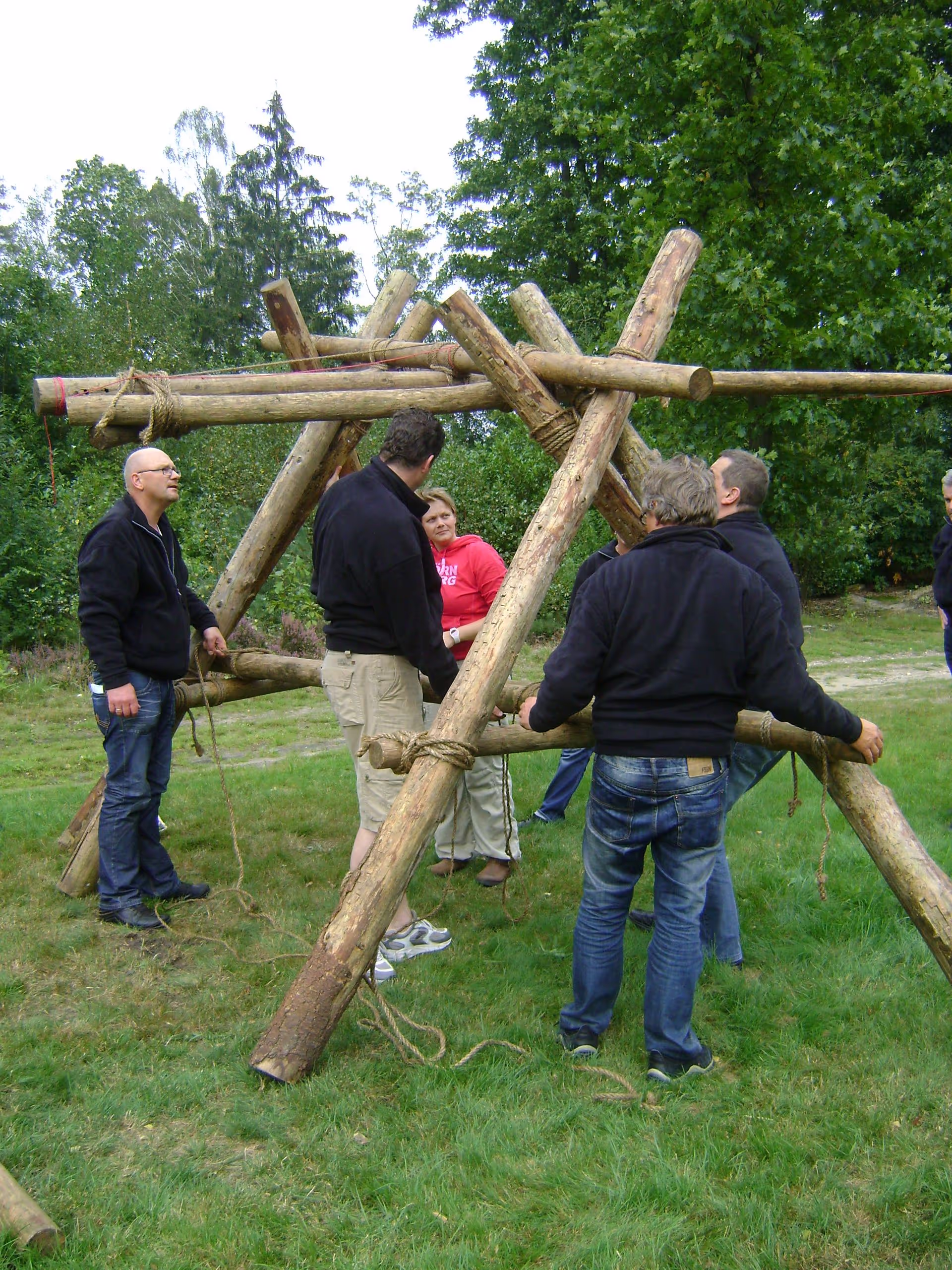 De katapult met dikke palen en touwen wordt gebouwd op een grasveld met circa zeven personen