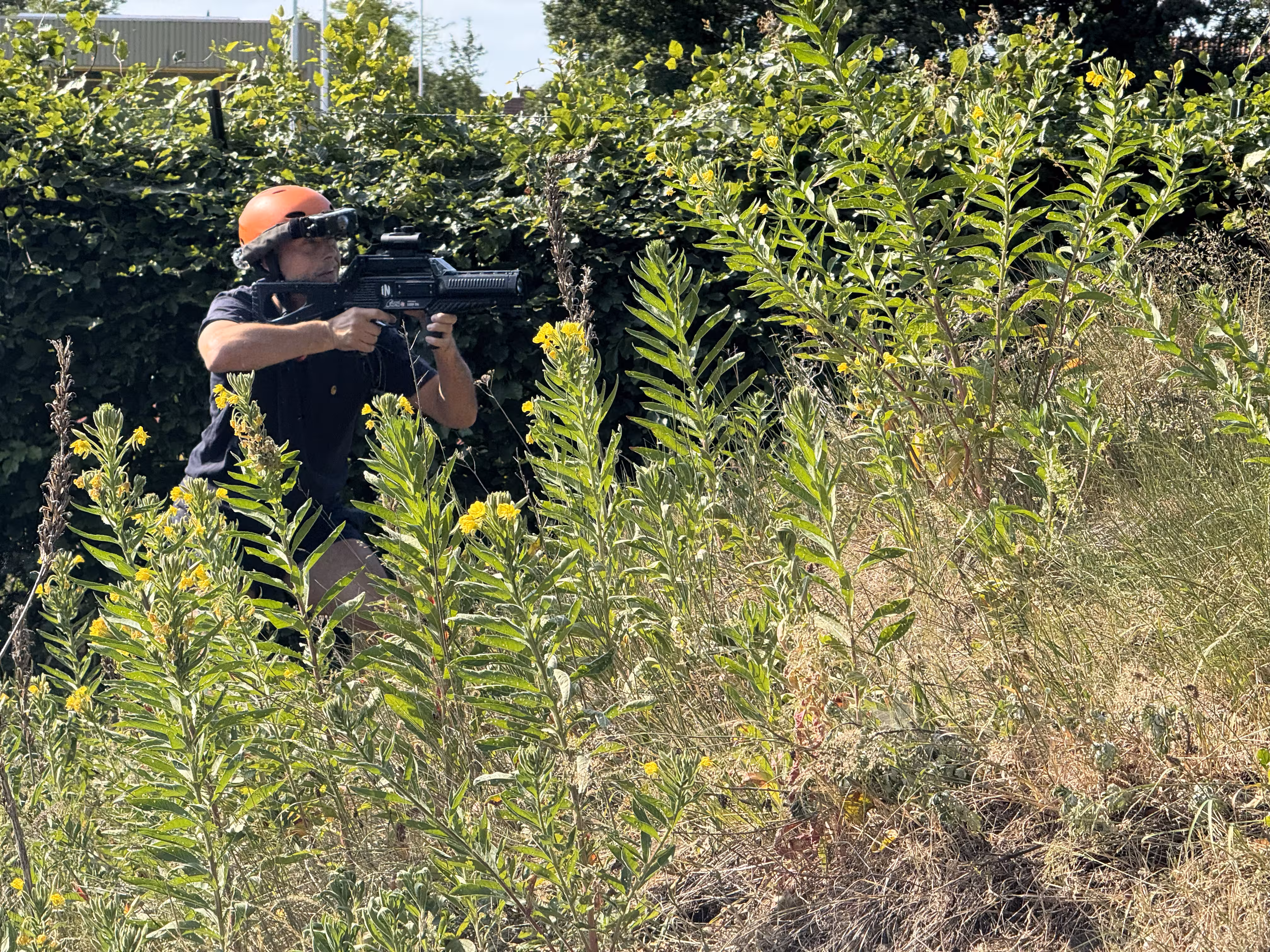 Een man met een oranje helm op is fanatiek bezig met richting met een lasergun tijdens de Outdoor Lasergame workshop