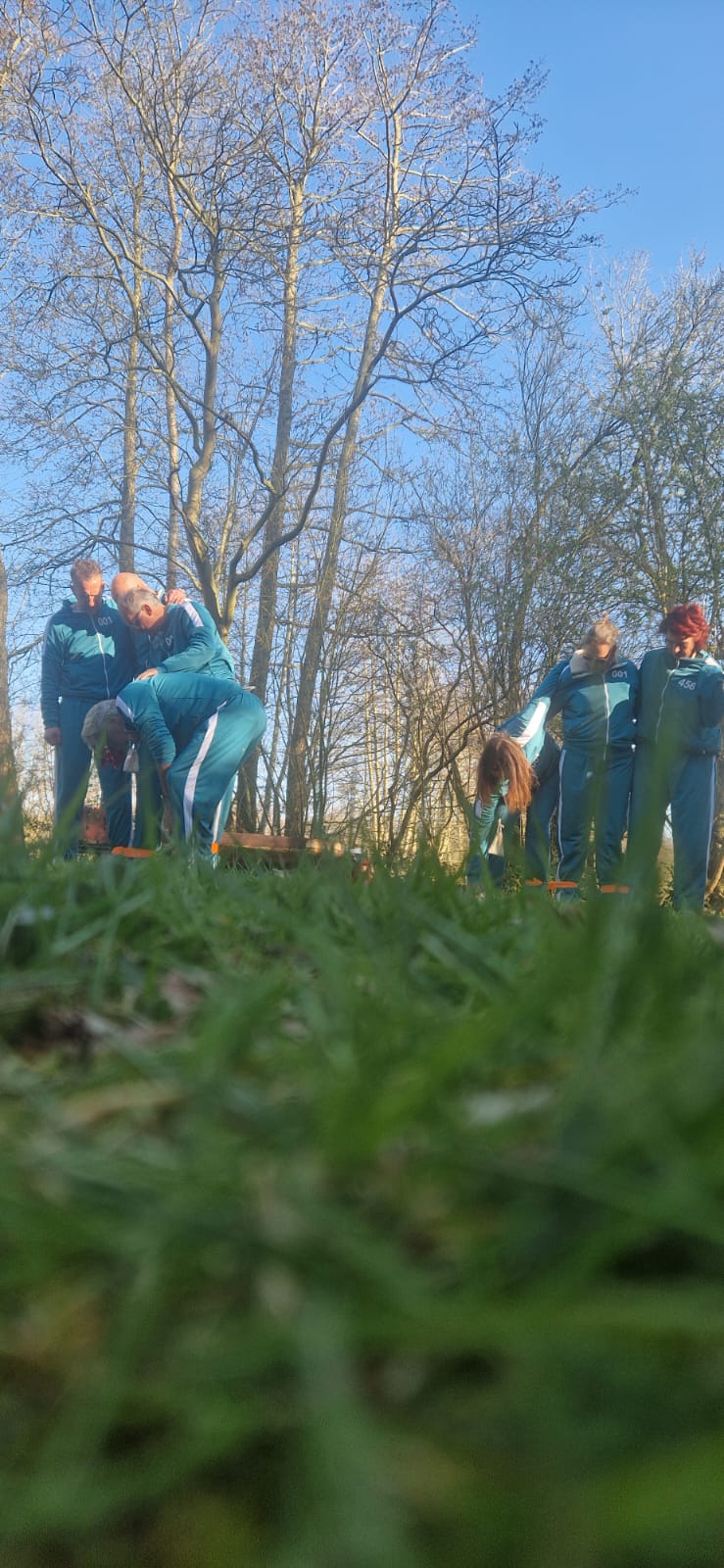 Op de voorgrond is gras te zien, daar achter zijn twee teams bezig met de Squid Game