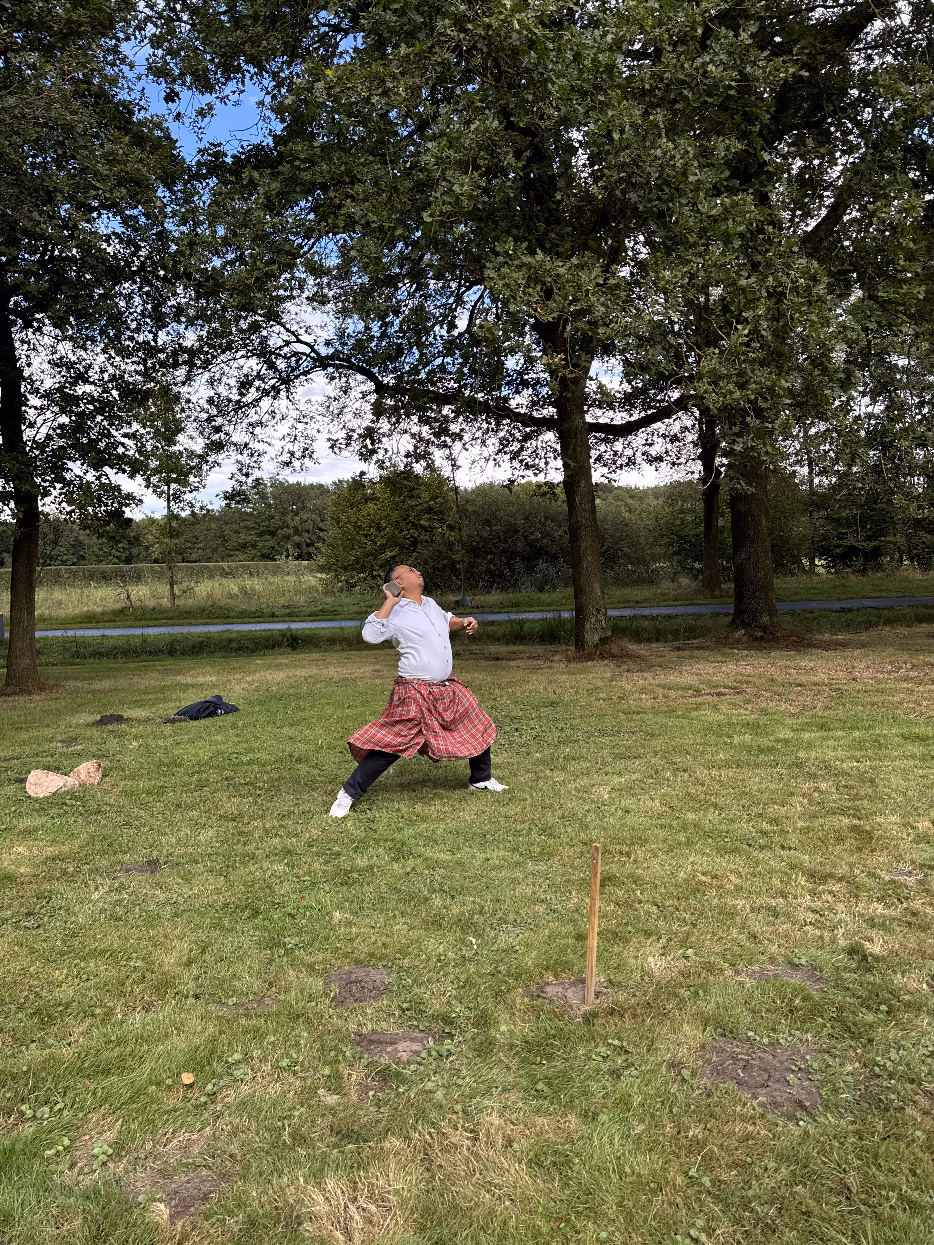 Een man met een witte blouse en rode rok gaat een kogel stoten