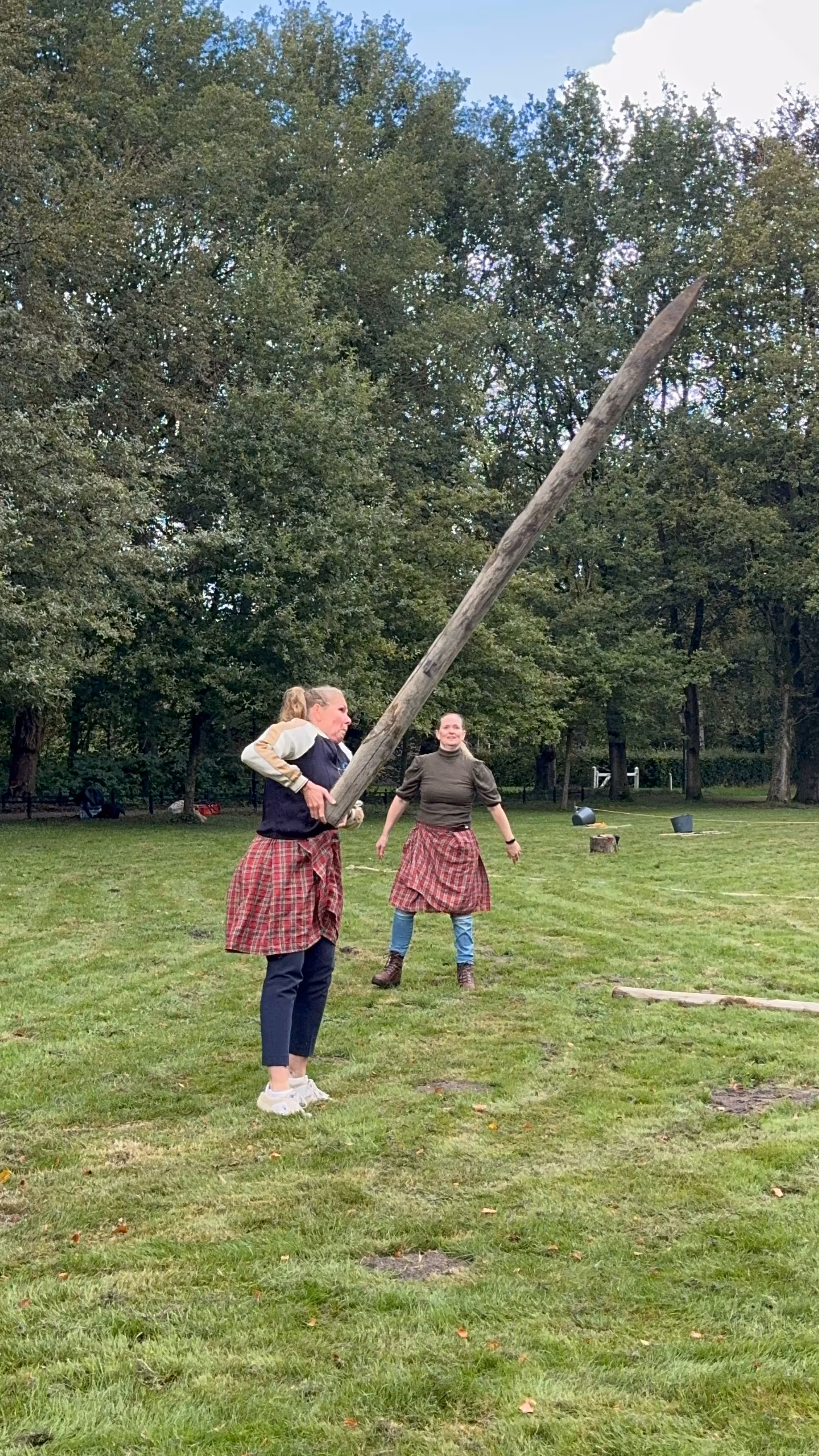 Een vrouw met een rode schotse rok werpt een grote houten balk weg
