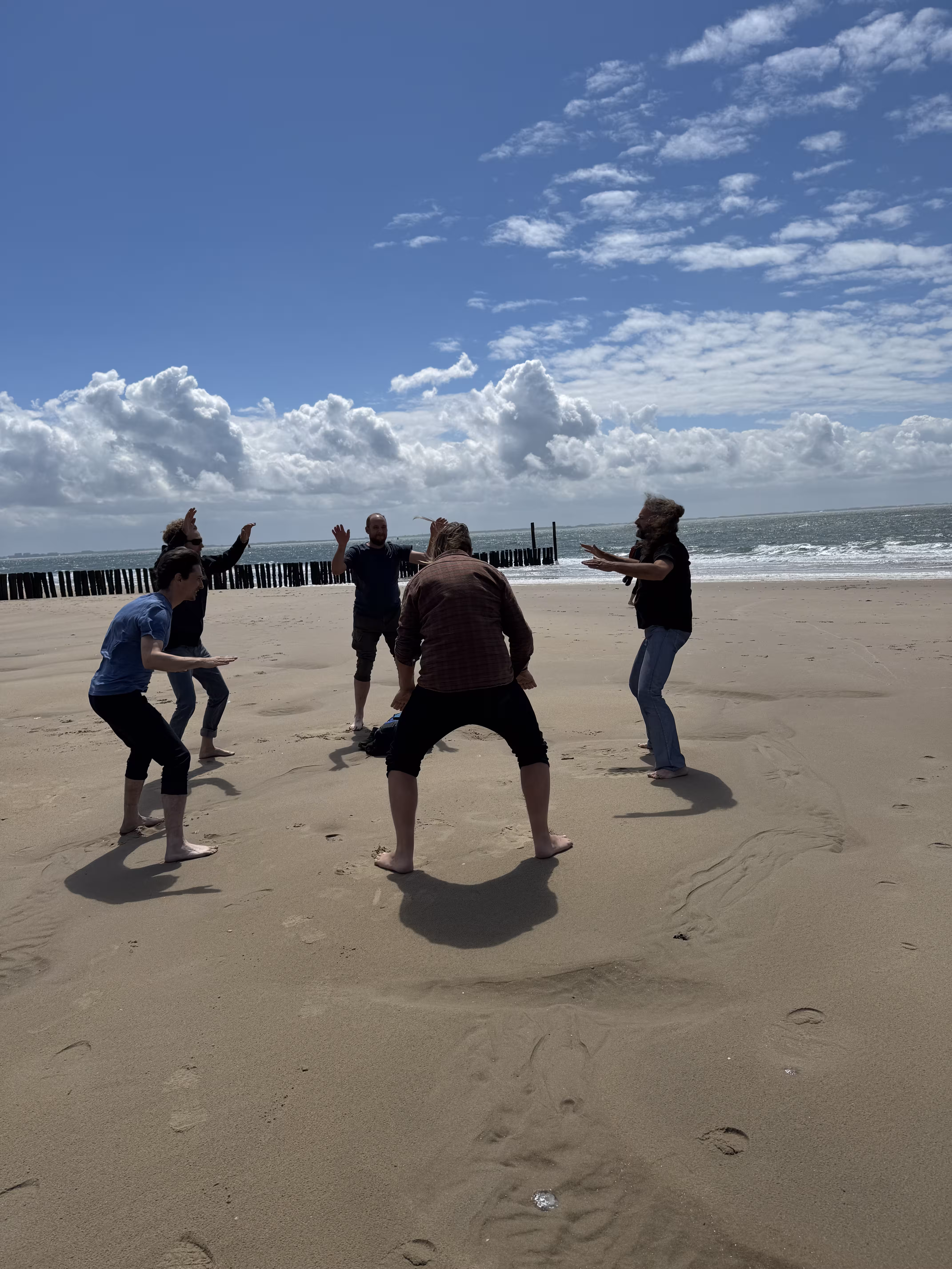 Op het strand staan vijf personen in een kring en doen de HAKA dans