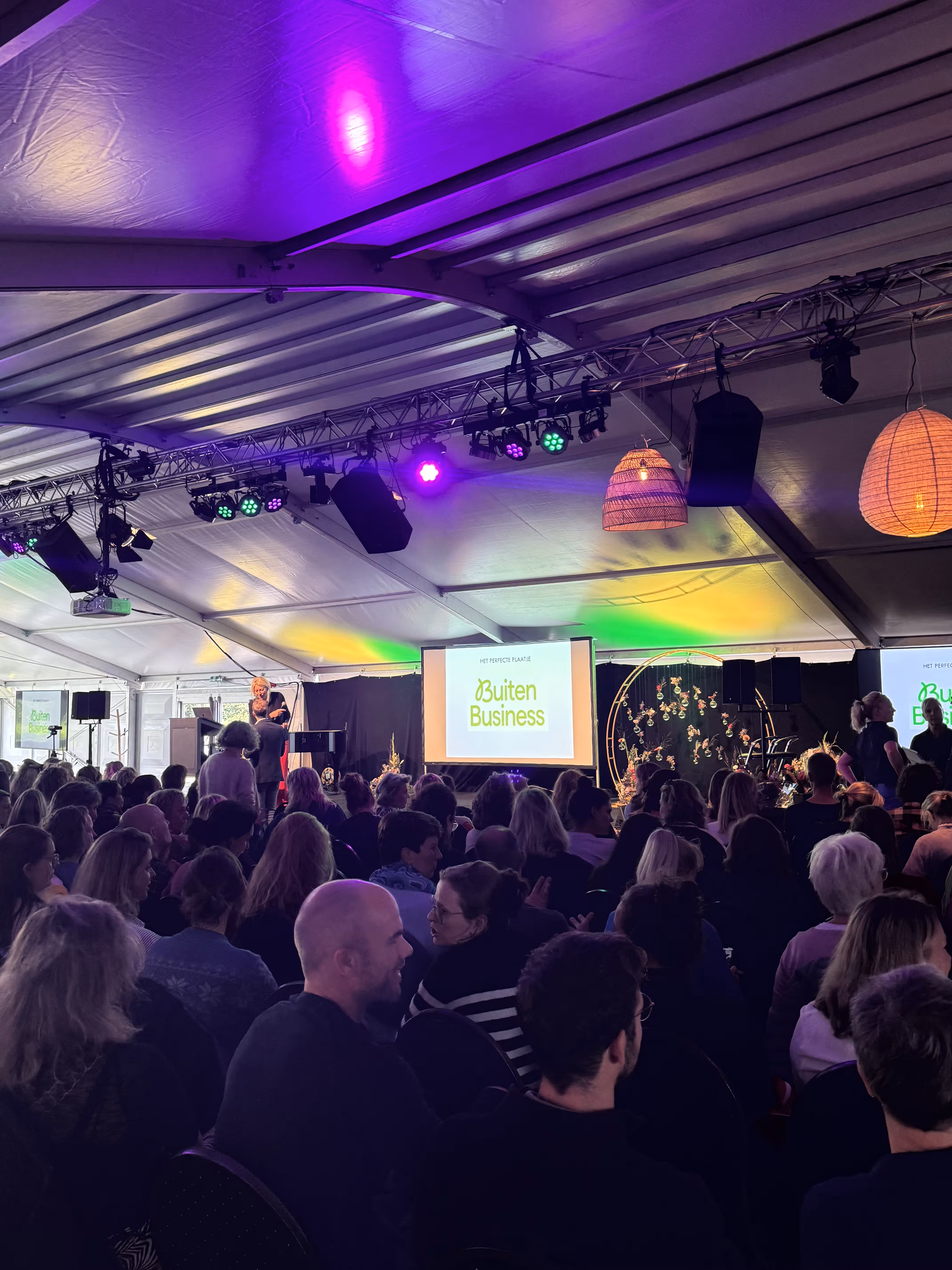 In een tent met gekleurde verlichting wordt door BuitenBusiness een presentatie gegeven op een beamer