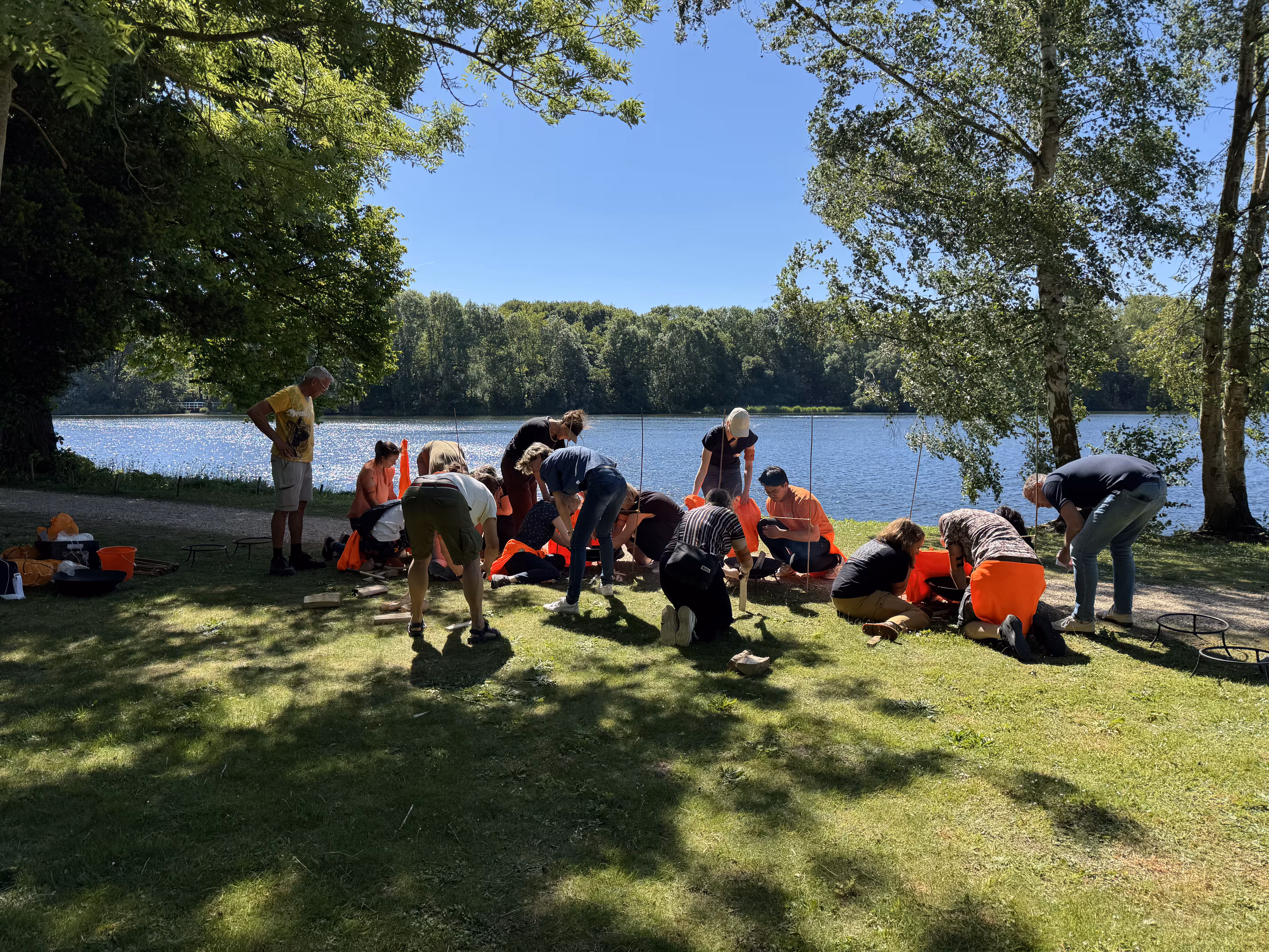 Op een grasveld bij een meer zitten verschillende teams op de grond om vuur te maken
