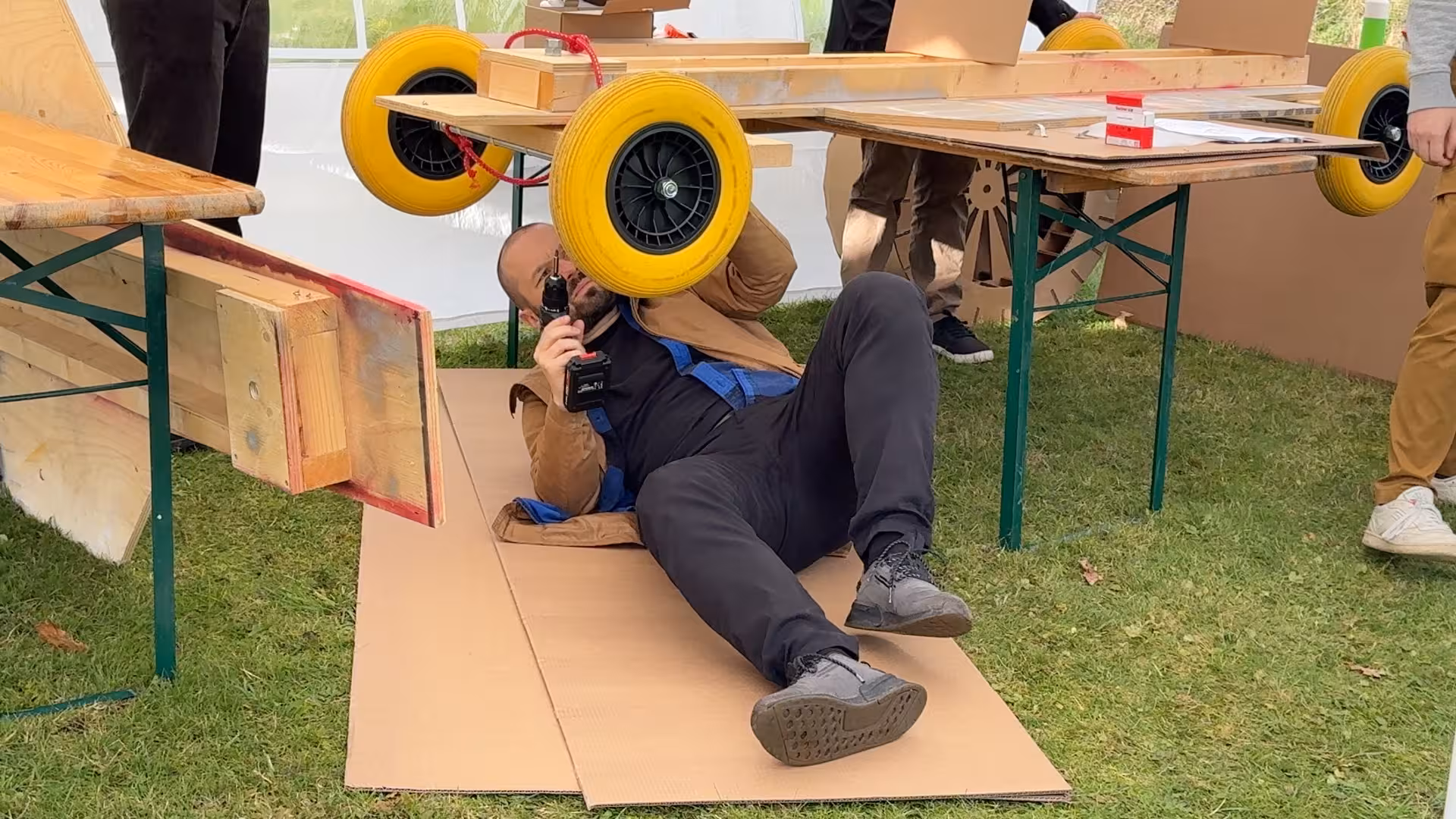 Een man ligt op een stuk karton en heeft een boormachine vast