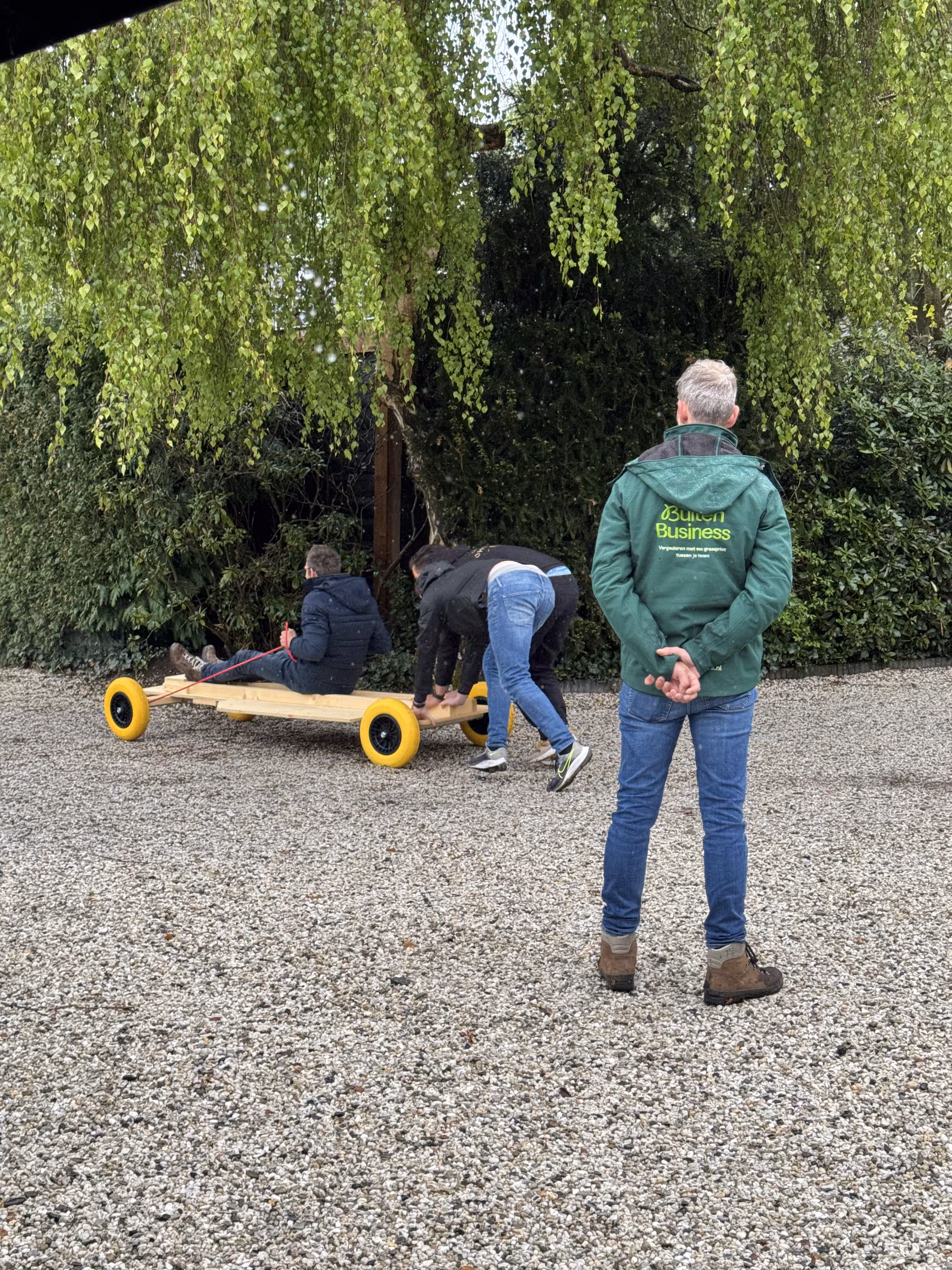 De BuitenBusiness instructeur kijkt hoe een F1 wagen door twee personen wordt geduwd over grind