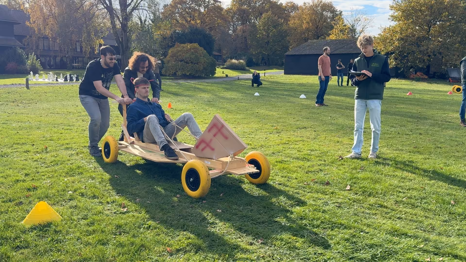 Zelfgemaakte F1 wagen nummer 77 rijdt over het grasveld met pionnen. De BuitenBusiness instructeur noteert de tijd