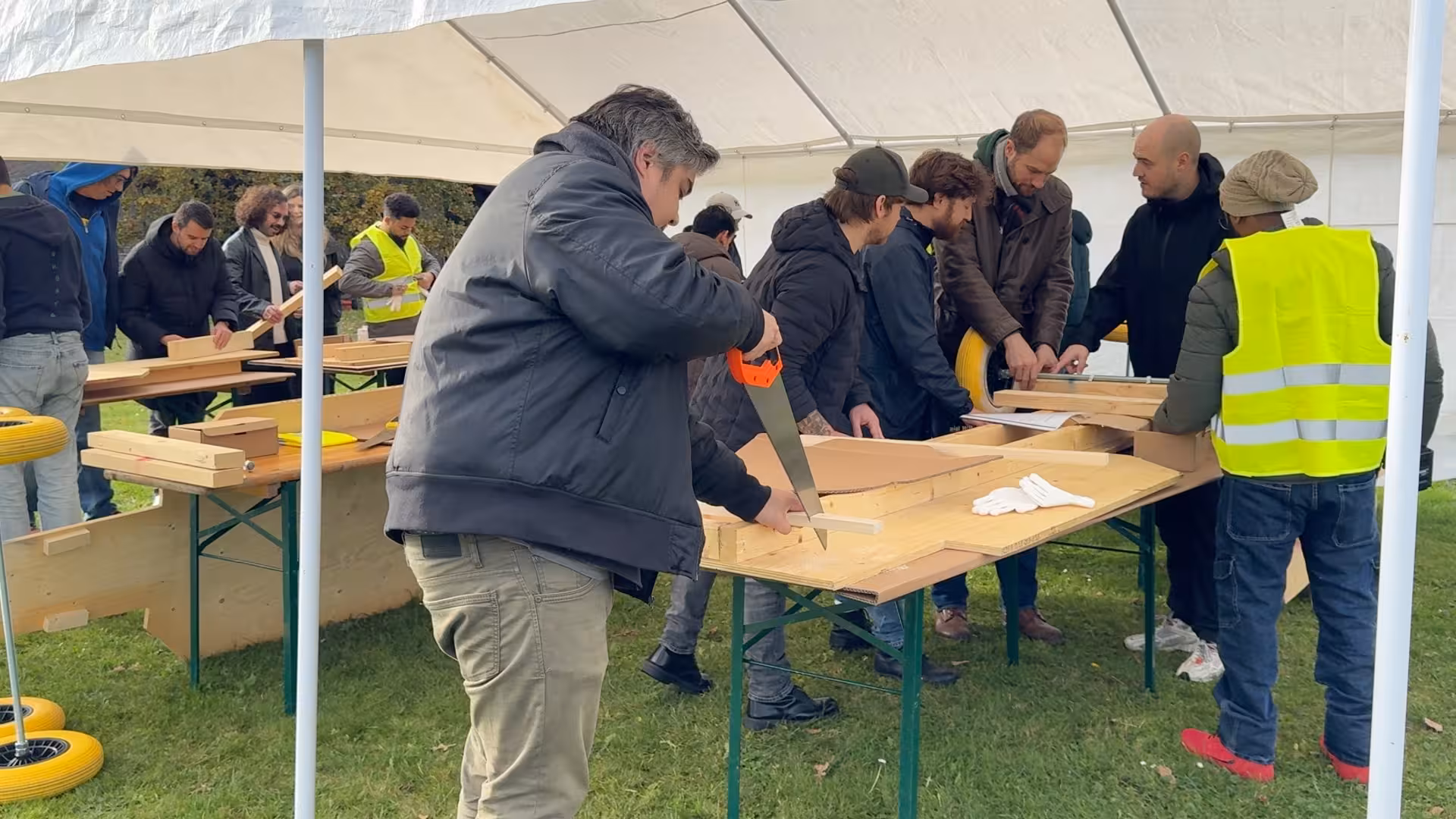 Een man zaagt door een dunne lat hout, dat op een biertafel ligt