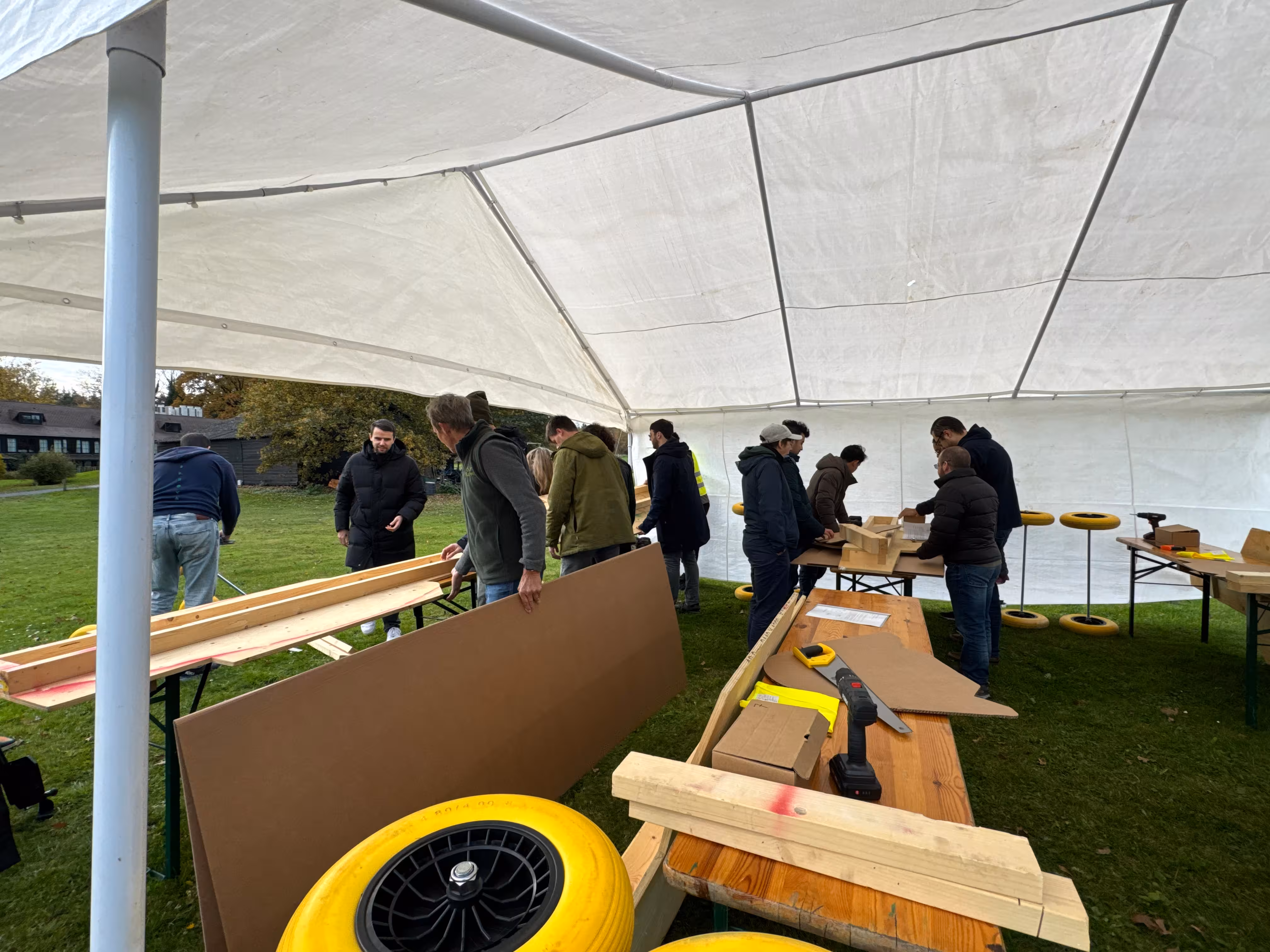 Onder een witte tent staan tafels waar de teams een zeepkist op bouwen.