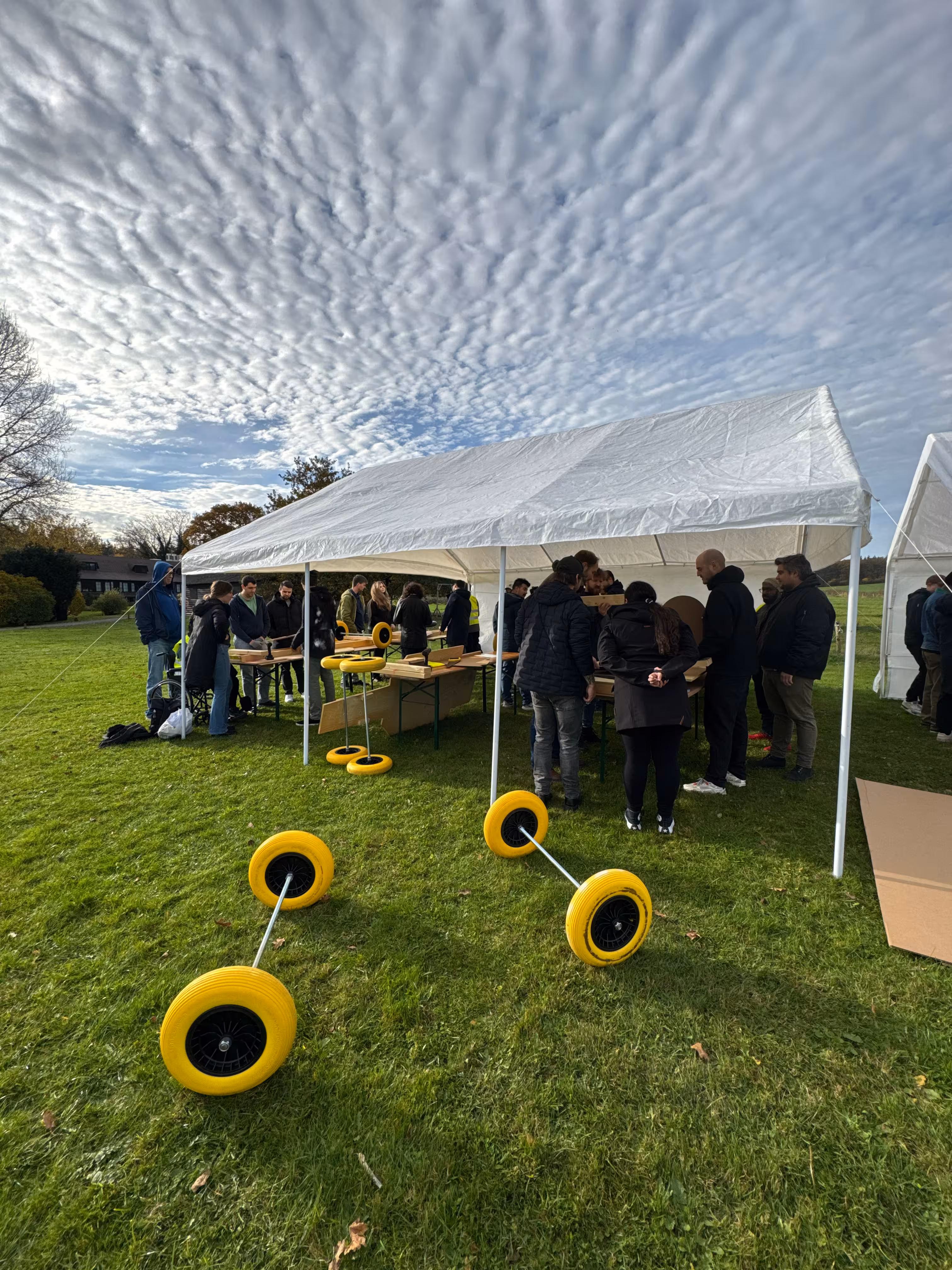 Op een bewolkte dag wordt in een witte tent gebouwd aan zeepkisten. Op het grasveld liggen gele wielen