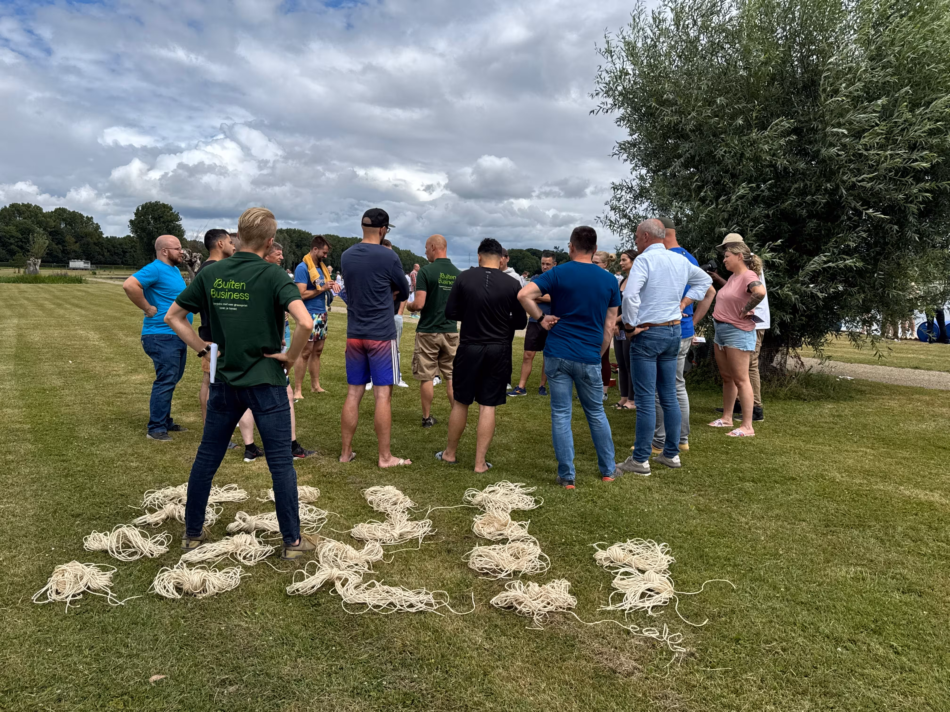 De BuitenBusiness instructeur staat bij de touwen en kijkt richting de groep die in een cirkel staan op een grasveld