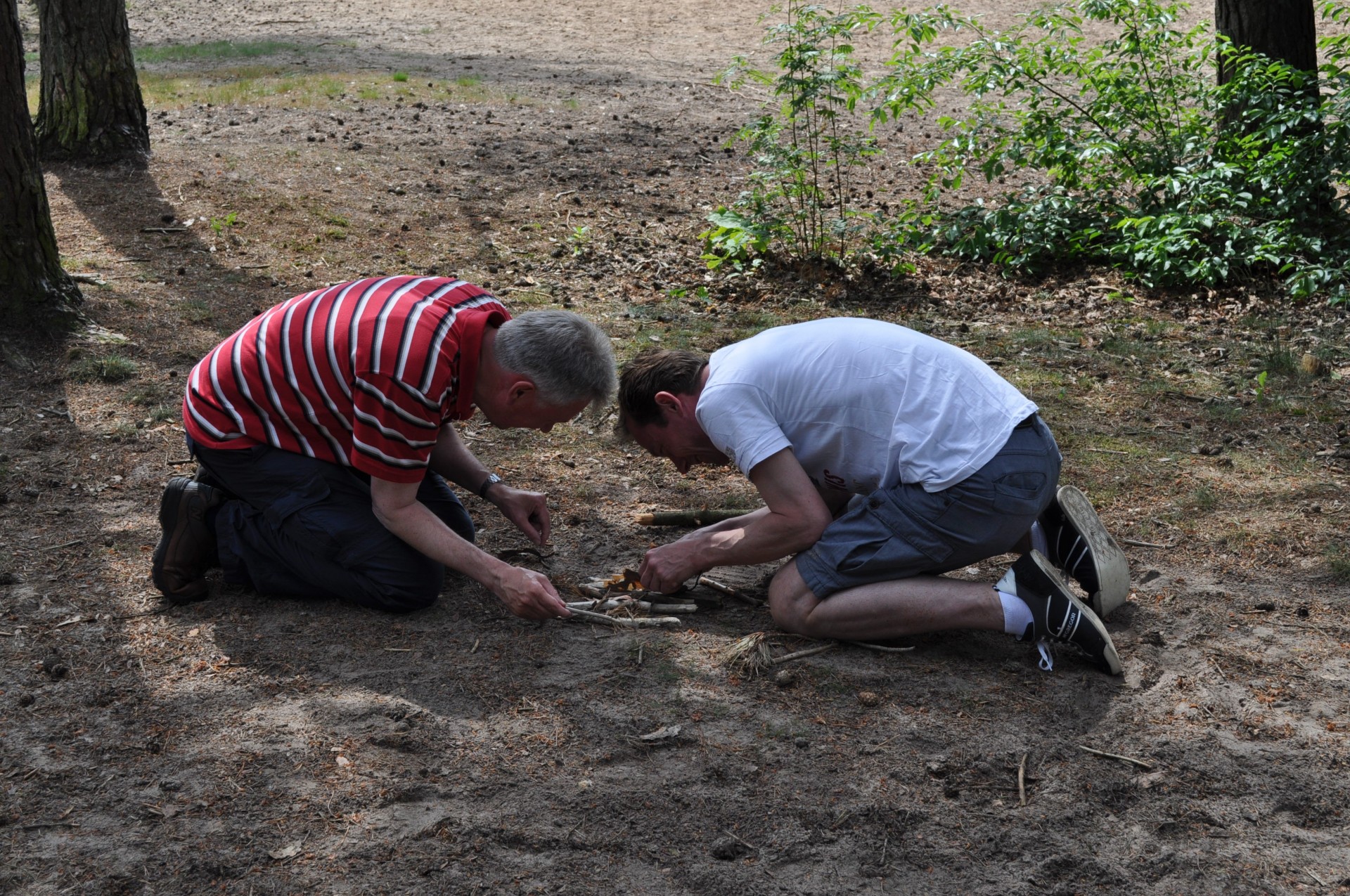 twee mannen zitten op de grond en proberen vuur te maken 