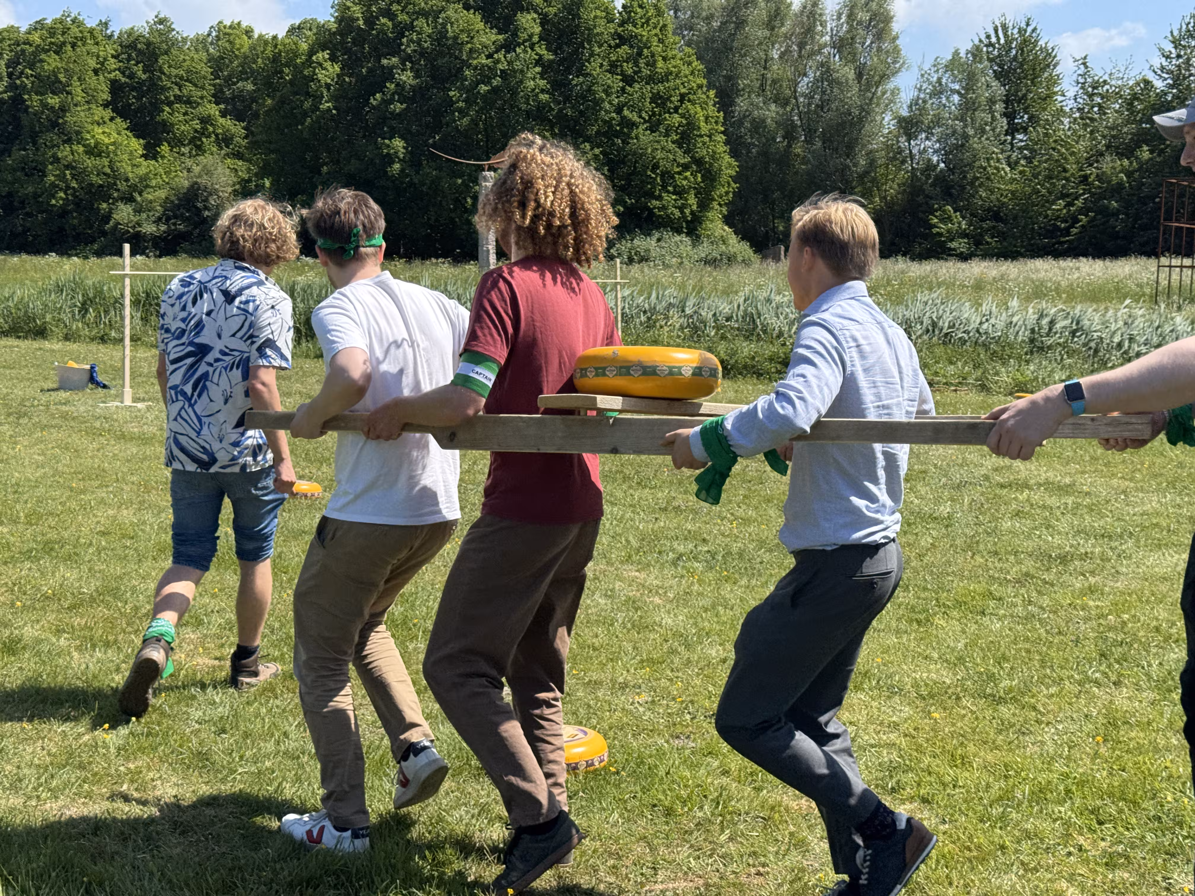 Drie mannen lopen tussen in een kaasdragen en rennen door een parcours van kazen op een grasveld