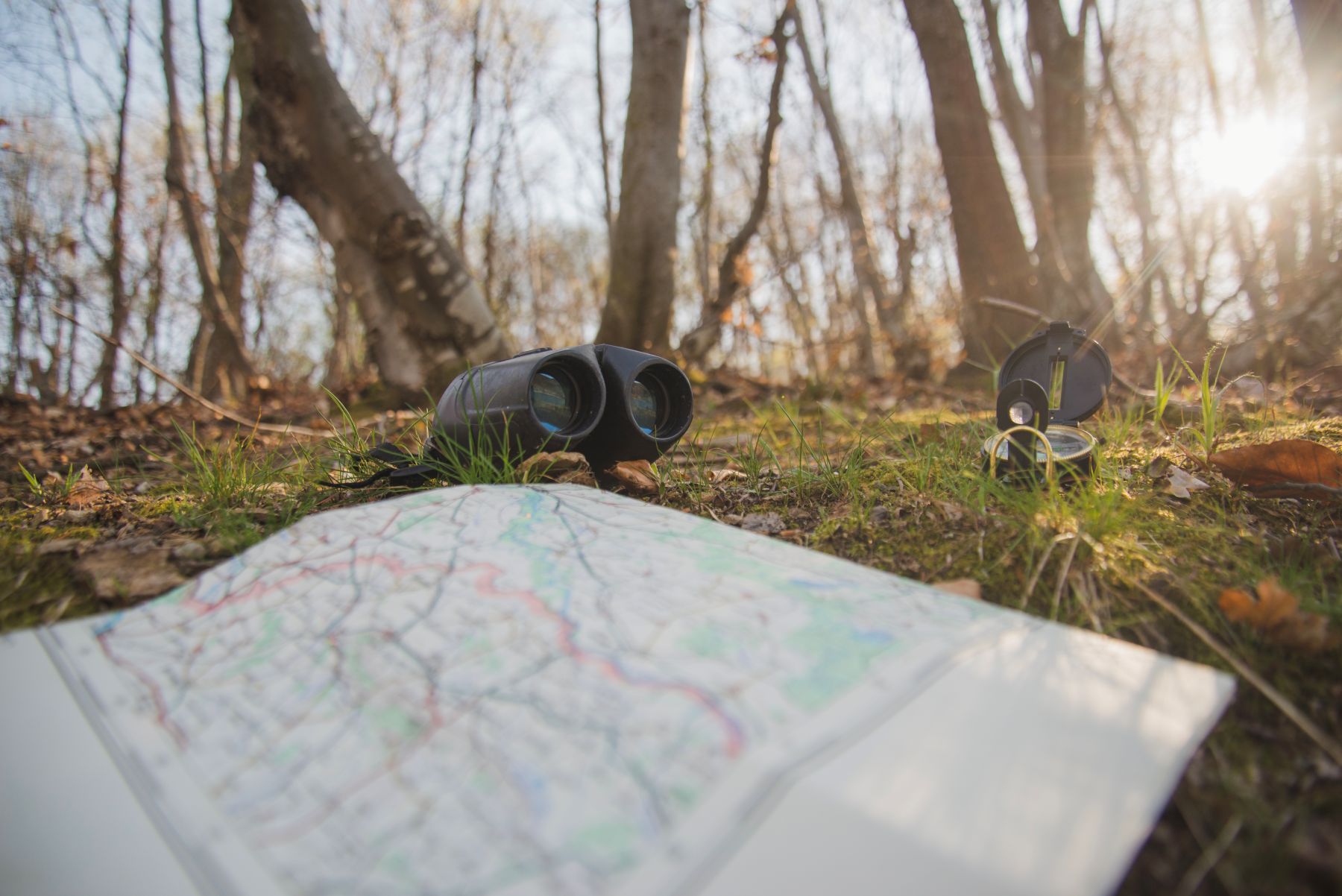 in het bos ligt een kaart, een verrekijker en kompas op de grond