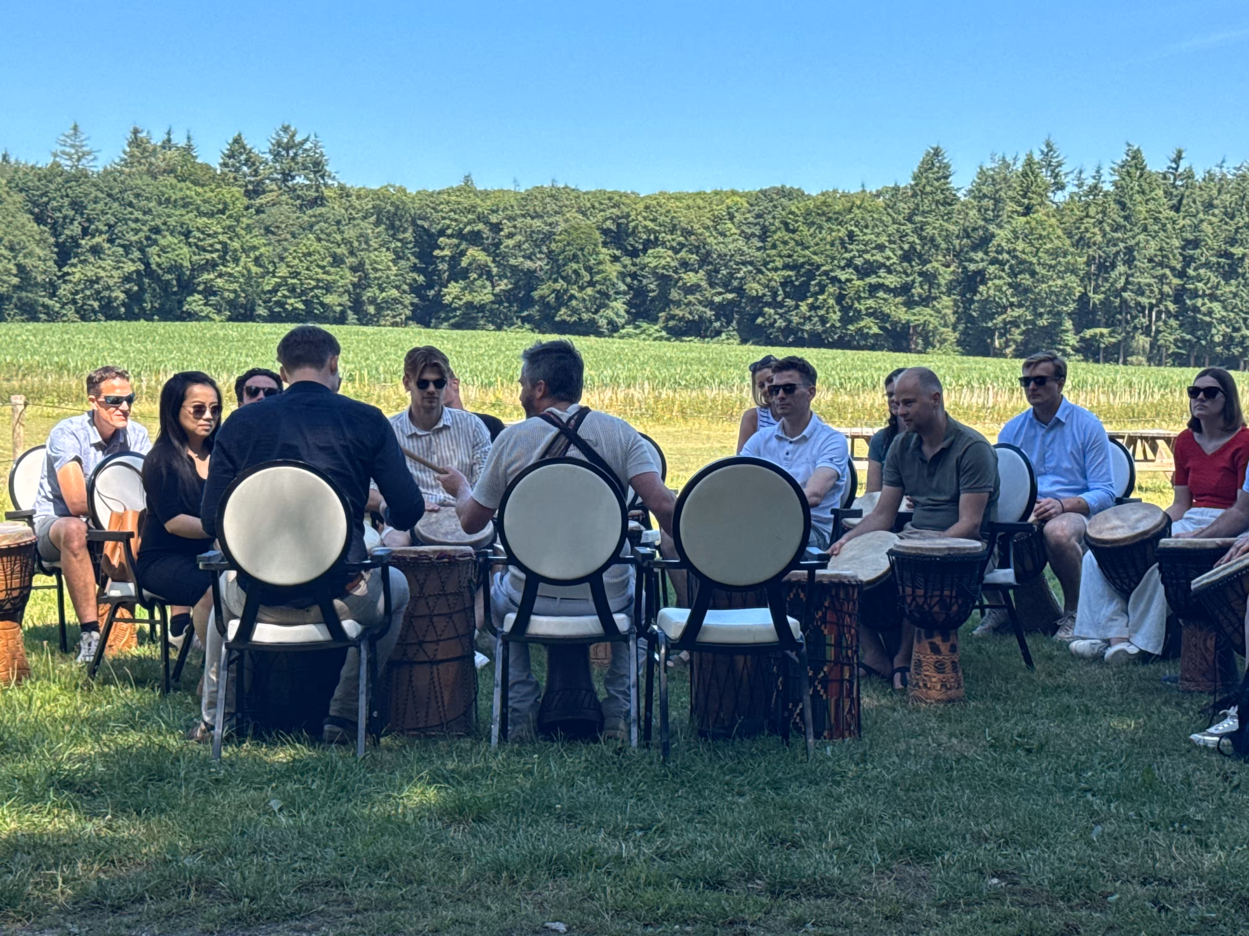 Op een grasveld zitten circa vijftien mensen bij elkaar met een djembé tijdens de percussie workshop