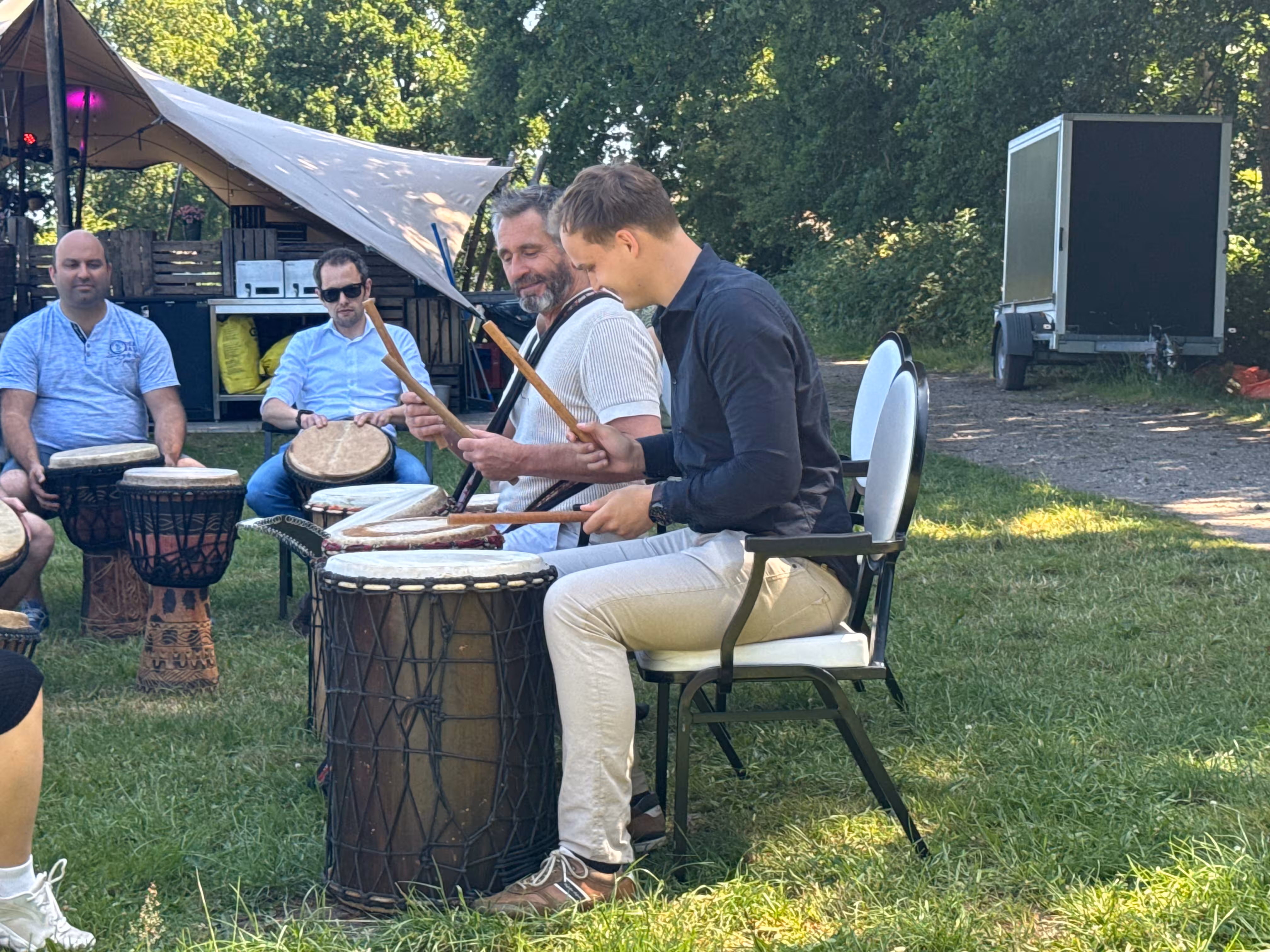 Met houten stokken slaan twee mannen die naast elkaar zitten op een bruine trommel
