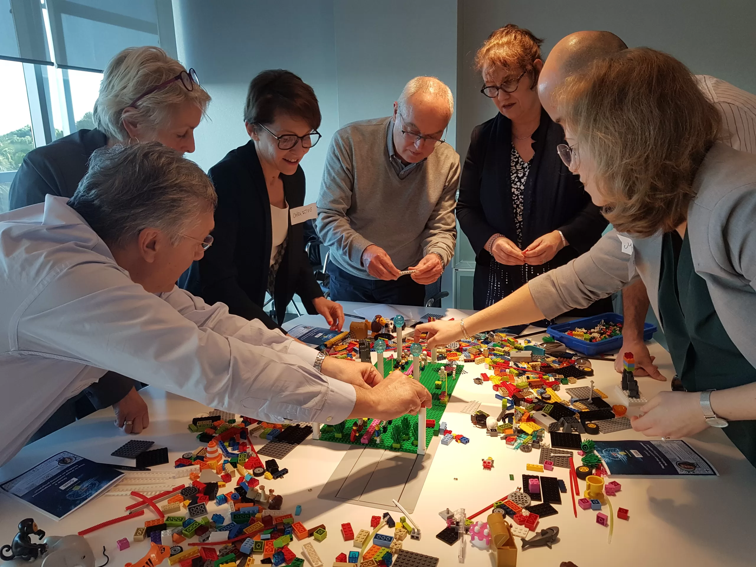 Zeven mensen staan om een tafel en bouwen met Lego Serious Play