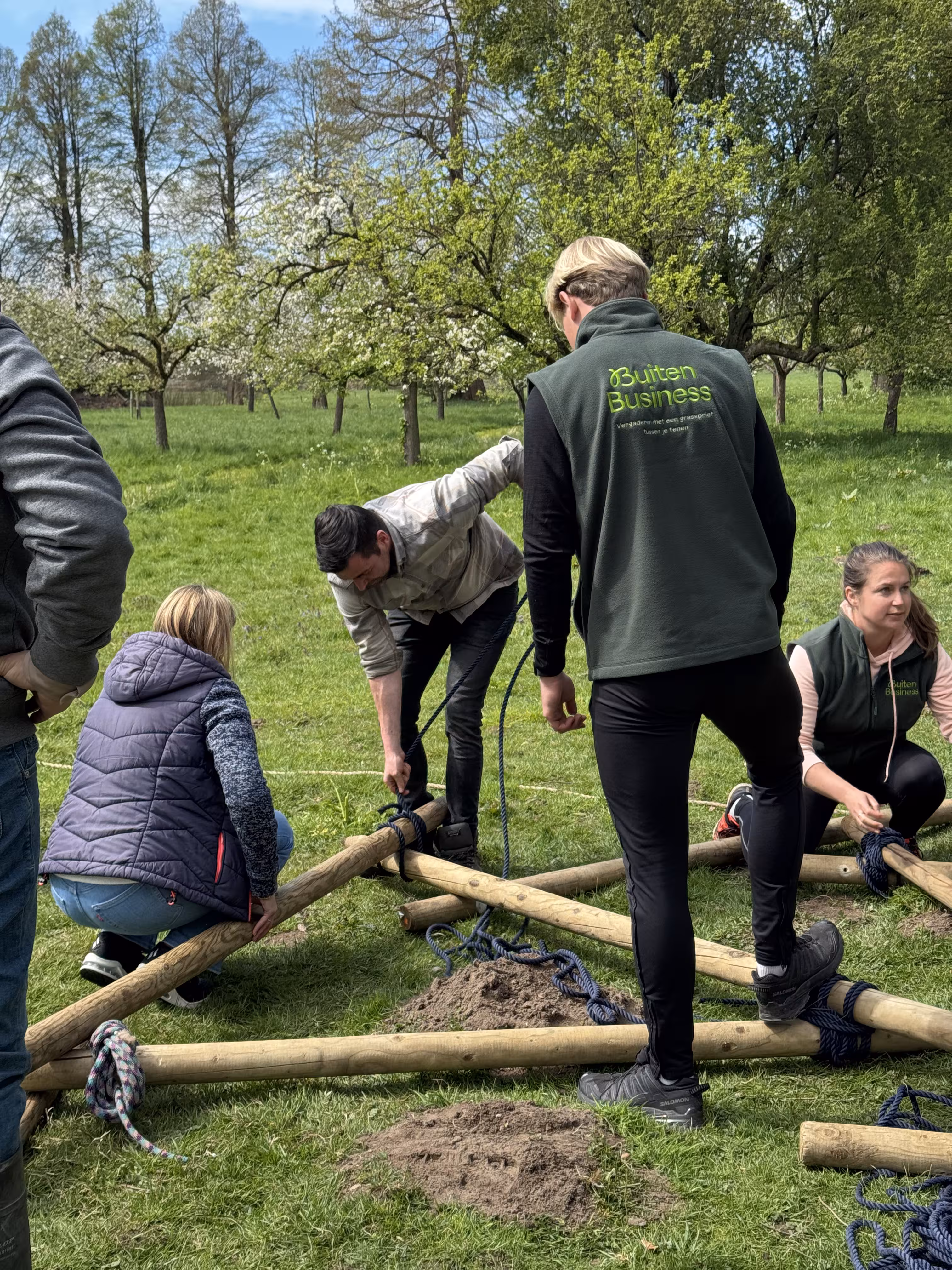 BuitenBusiness instructeur kijkt naar een man die een touw knoopt om twee houten palen