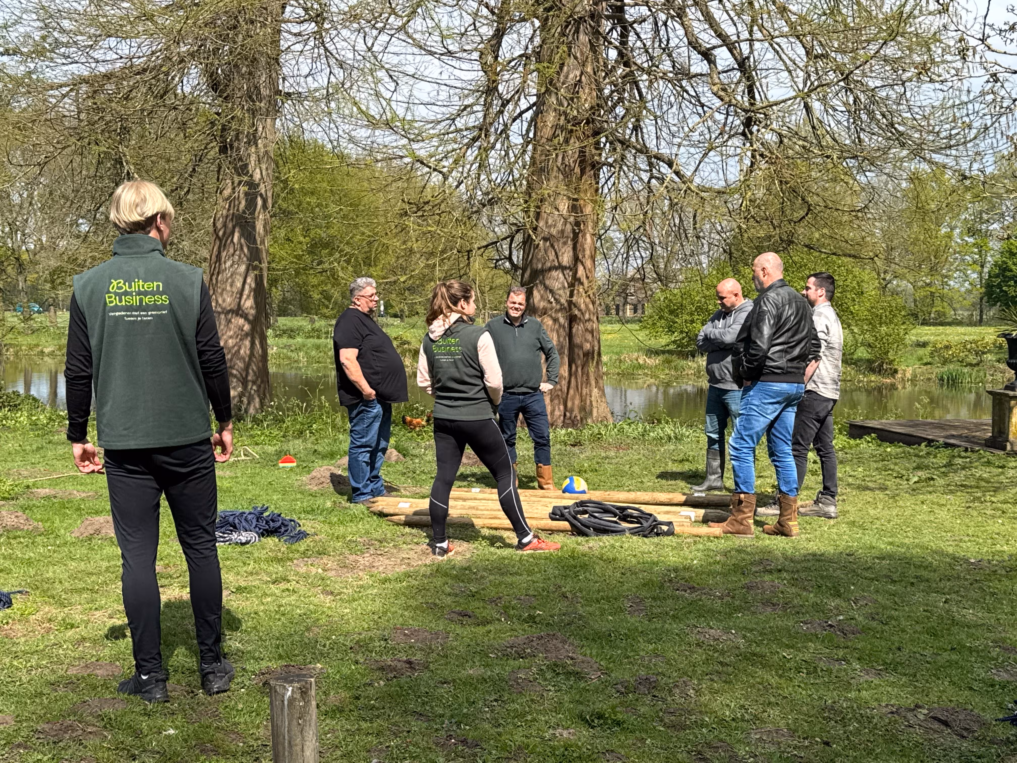 Twee BuitenBusiness instructeurs geven uitleg over de katapult materialen die op het grasveld klaarliggen