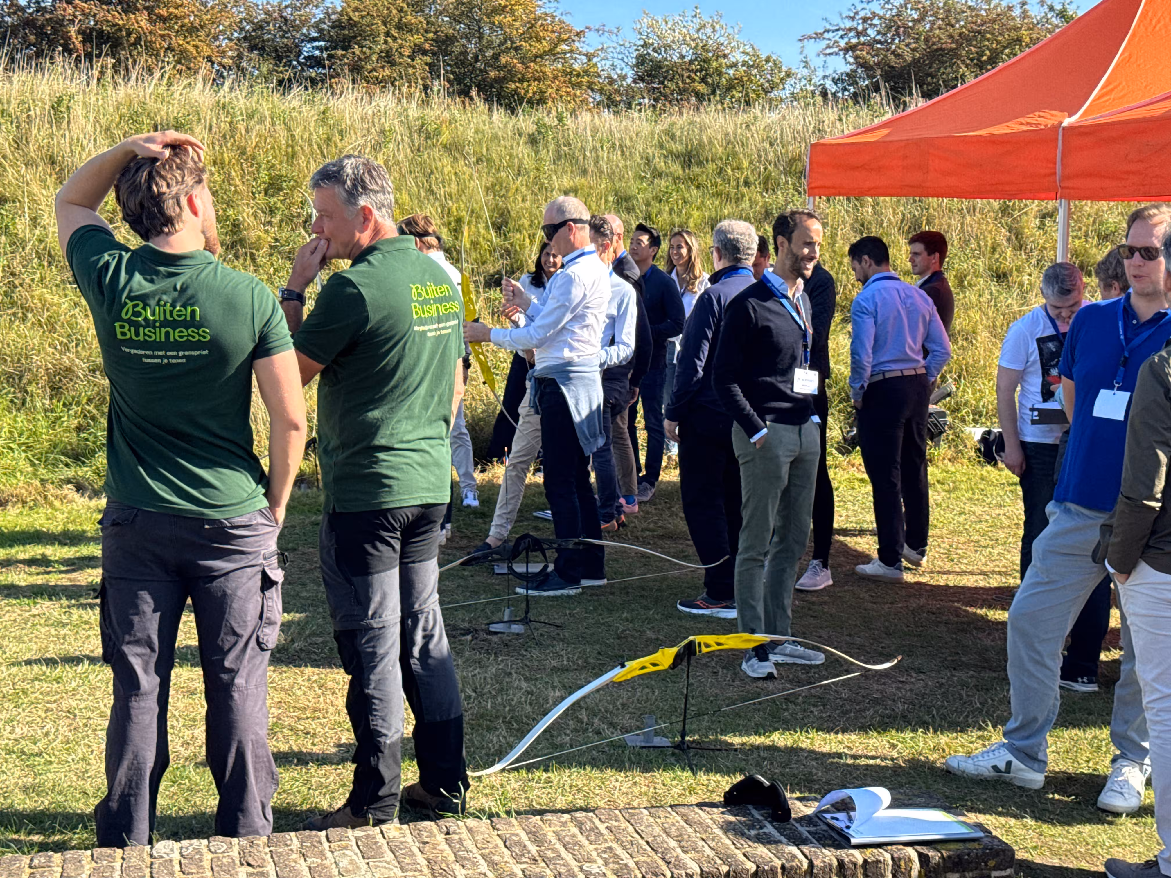 De twee BuitenBusiness instructeurs overleggen met elkaar. Op de achtergrond is de groep bezig met het blind boogschieten