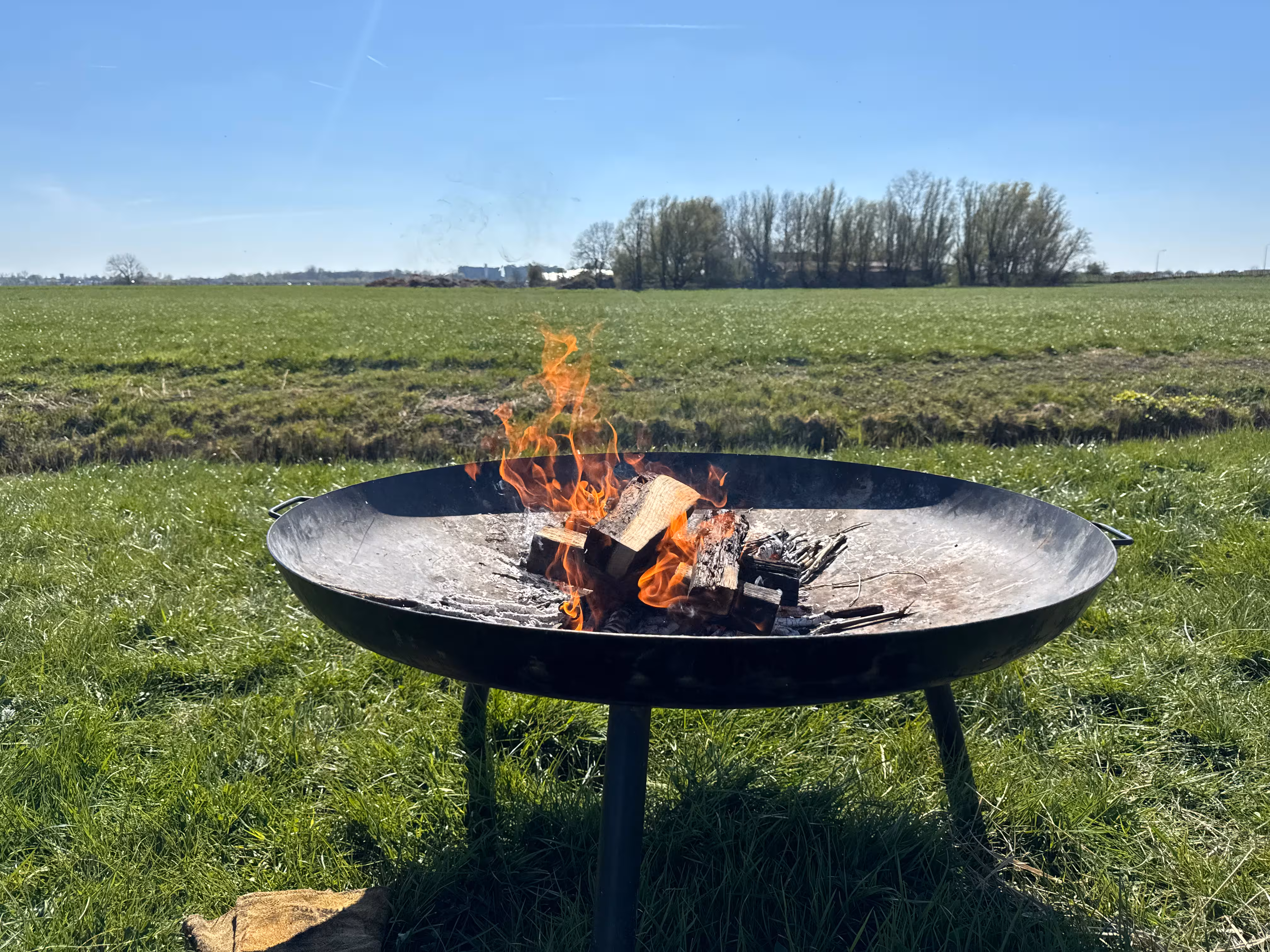 Een vuurschaal met een brandend vuur staat op een weiland