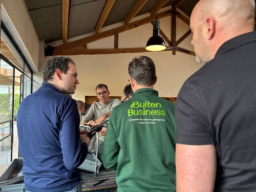 In een binnenruimte legt de BuitenBusiness instructeur een kettingreactie uit aan een groep mannen