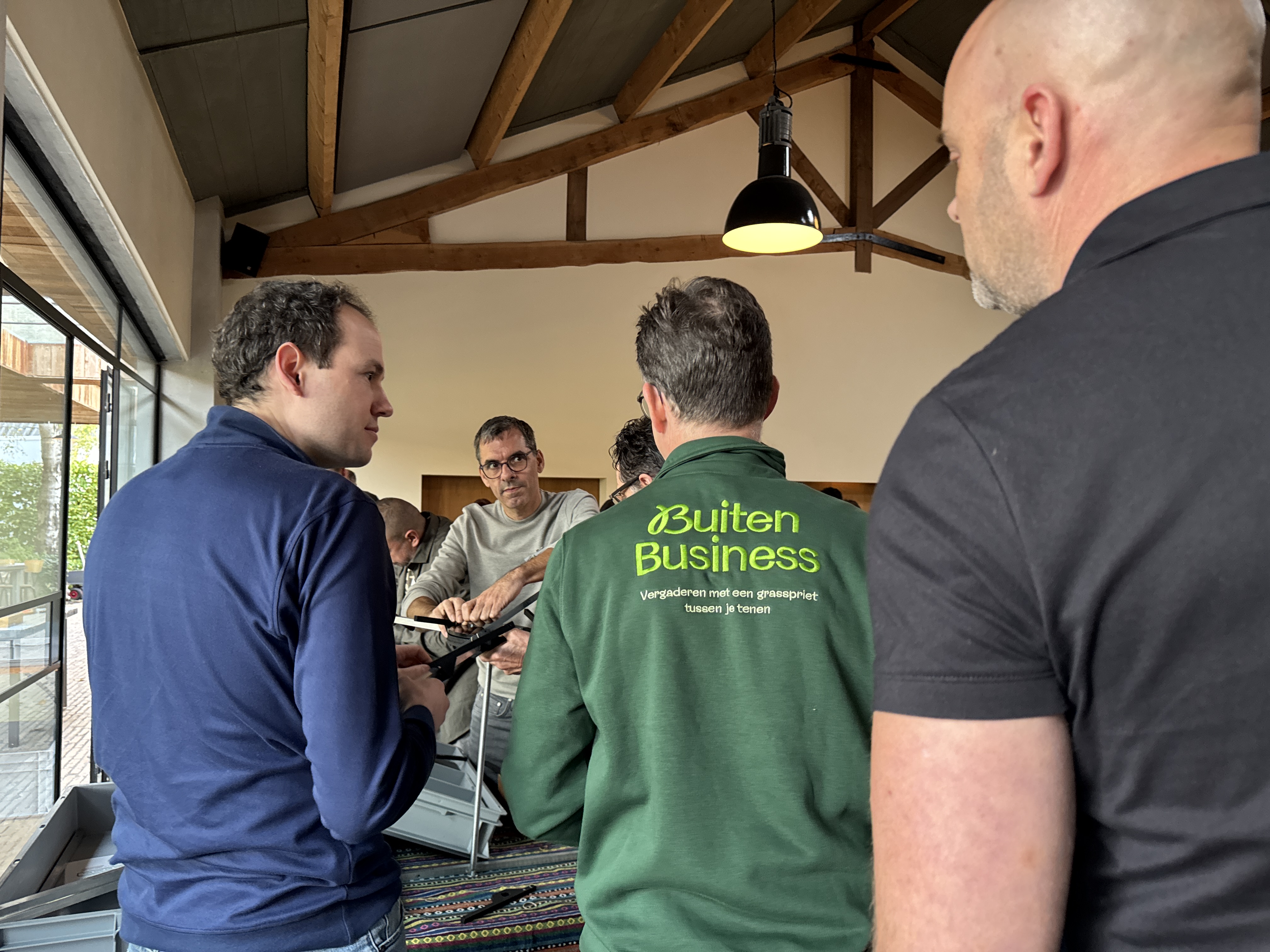 In een binnenruimte legt de BuitenBusiness instructeur een kettingreactie uit aan een groep mannen