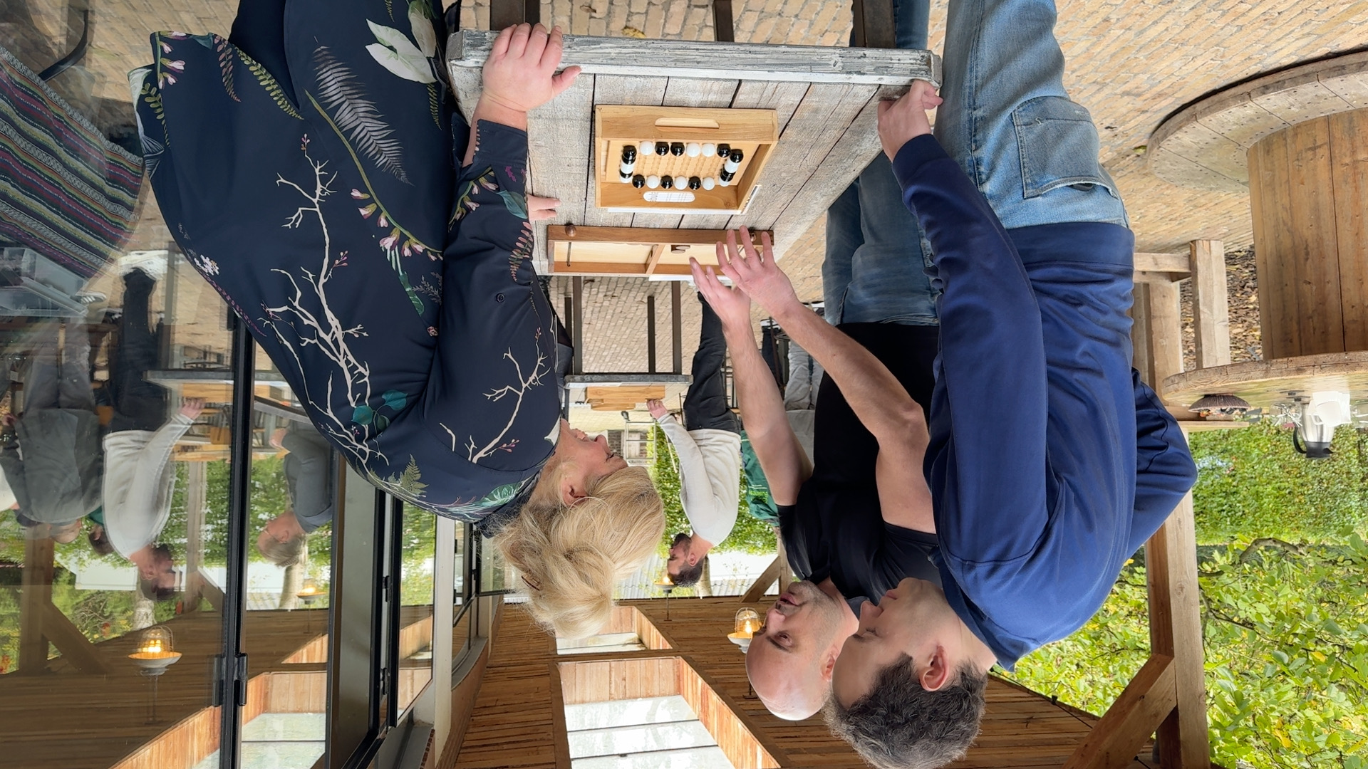 Drie personen staan om een tafel met daarop een houten spel met witte en zwarte knikkers