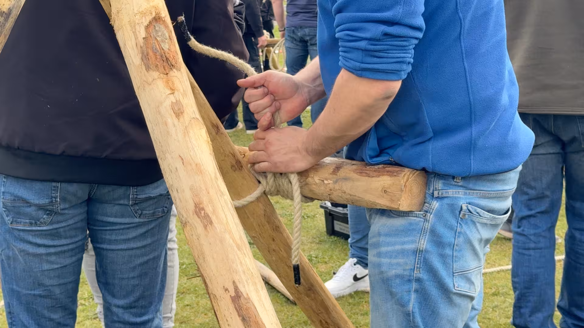 Een deelnemer met een blauwe trui legt een knoop om twee houten balken te bevestigen