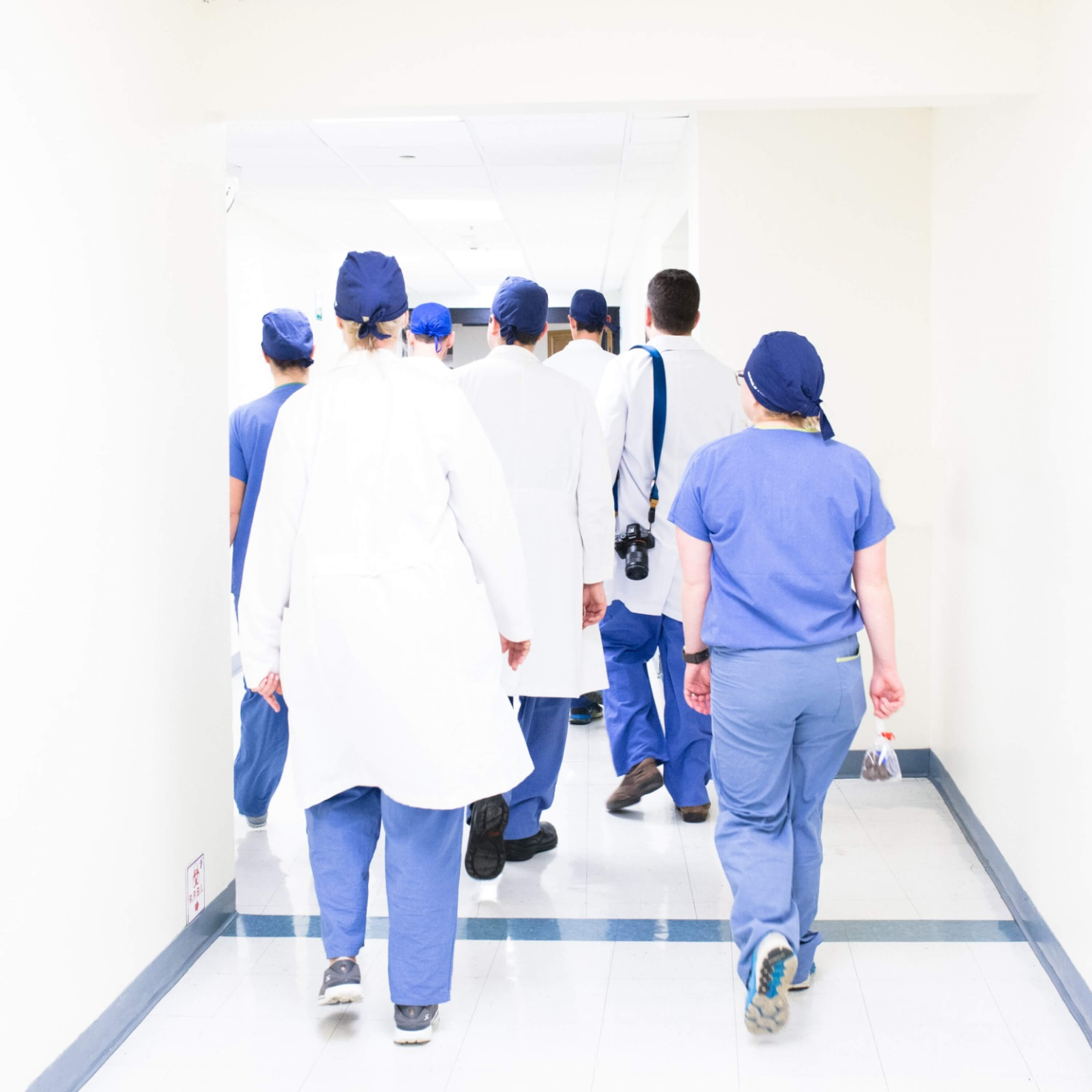 7 doctors and nurses walk down a corridor with their backs to us. Photo.