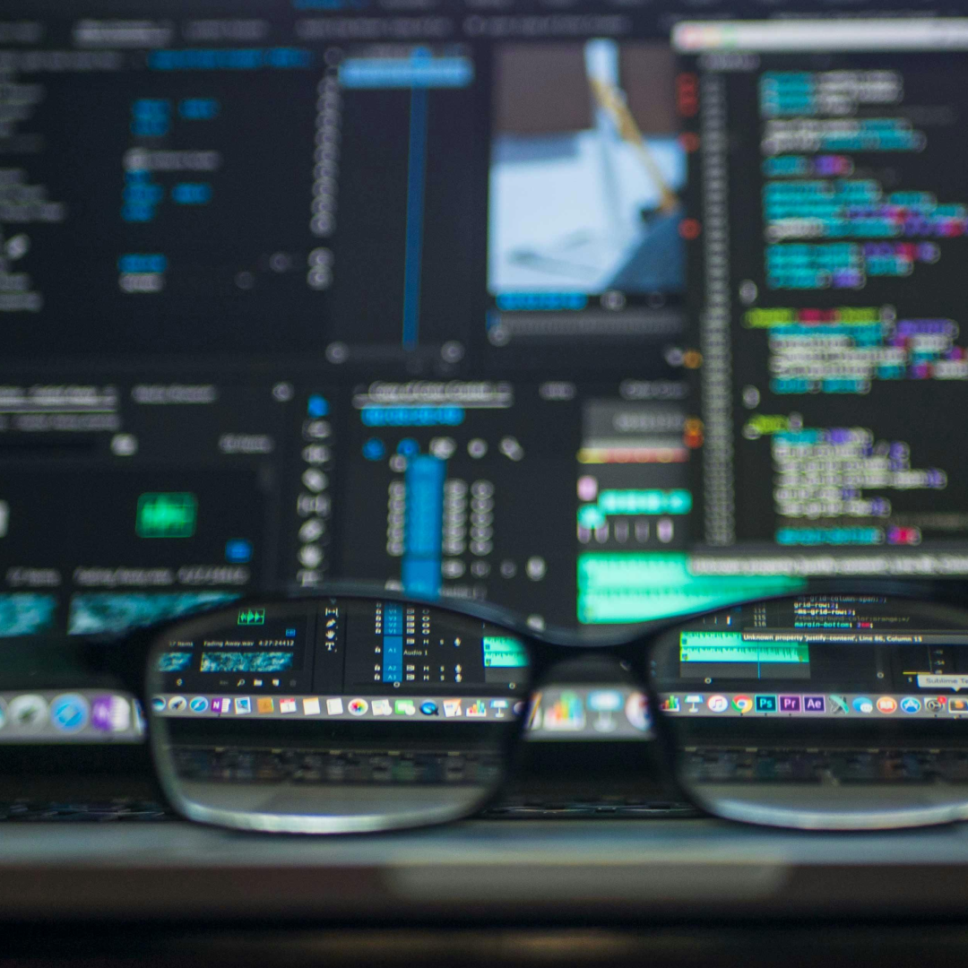 Close-up of eyeglasses in front of a laptop screen displaying colorful code and data dashboards, symbolizing software development and data analysis.