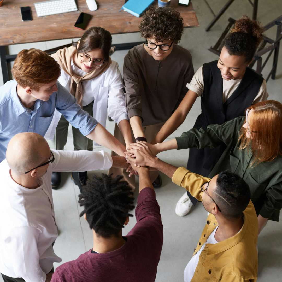 Project team members stand in a circle with hands stacked together, representing successful collaboration and cross-functional teamwork.
