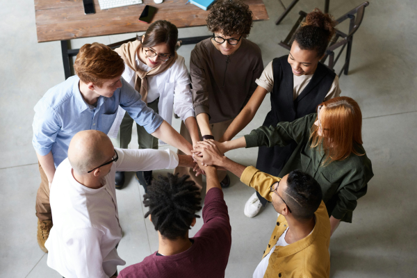 Project team members stand in a circle with hands stacked together, representing successful collaboration and cross-functional teamwork.