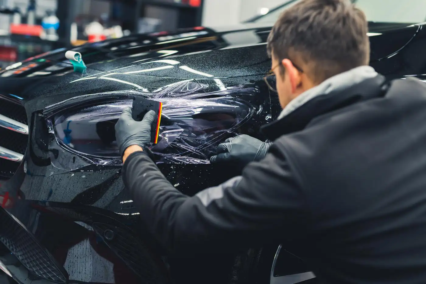 Technician installing paint protection film on the bumper of a Mercedes-Benz E-Class.