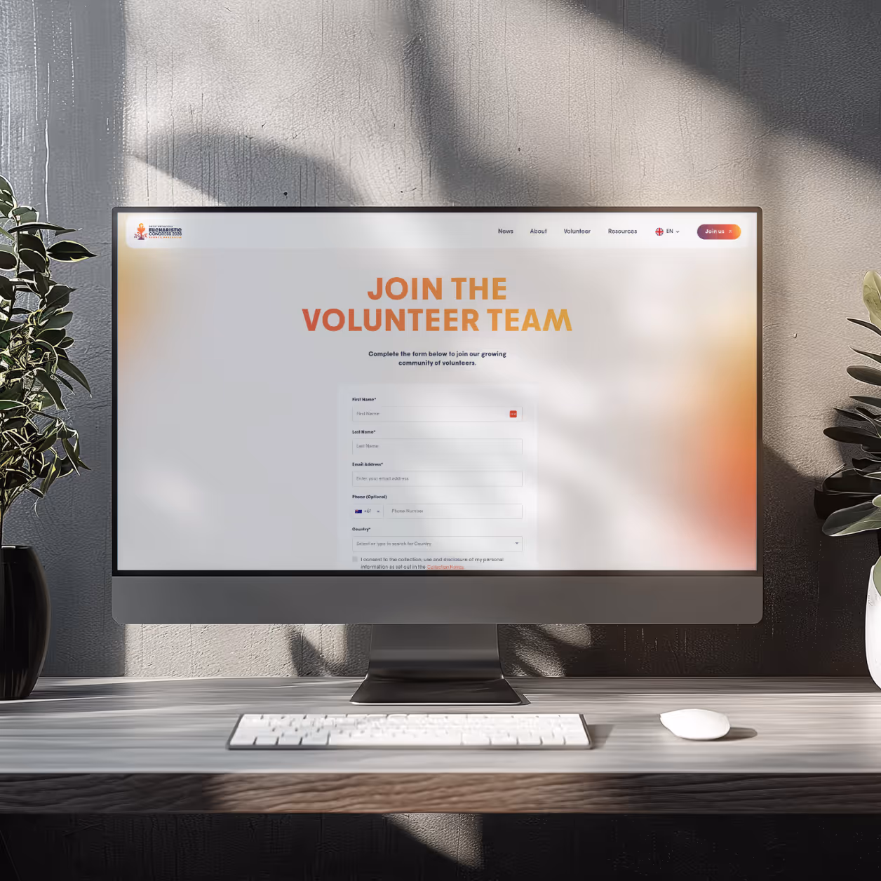Computer screen on desk showing a volunteer sign-up form with keyboard, mouse, and plants nearby.