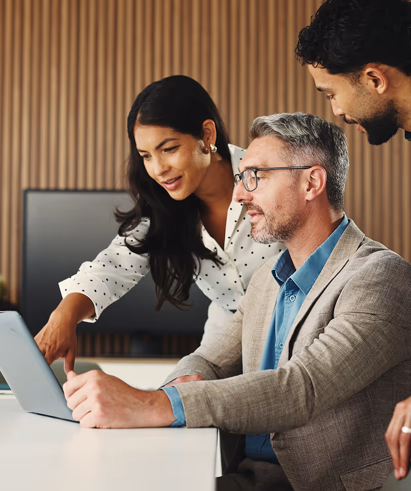 Three coworkers reviewing content on a tablet at a white desk in an office with wood paneling.