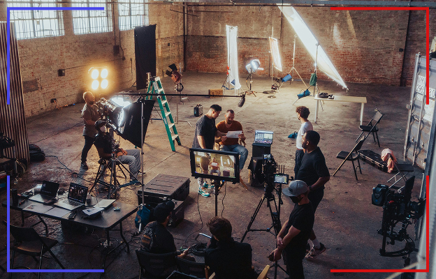 Film crew setting up cameras, lights, and equipment in a spacious industrial-style studio with brick walls and large windows.