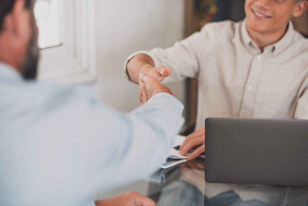 Two men shaking hands at a desk during a business meeting. Image related to 'How to Hire Niche IT Remote Staff'.