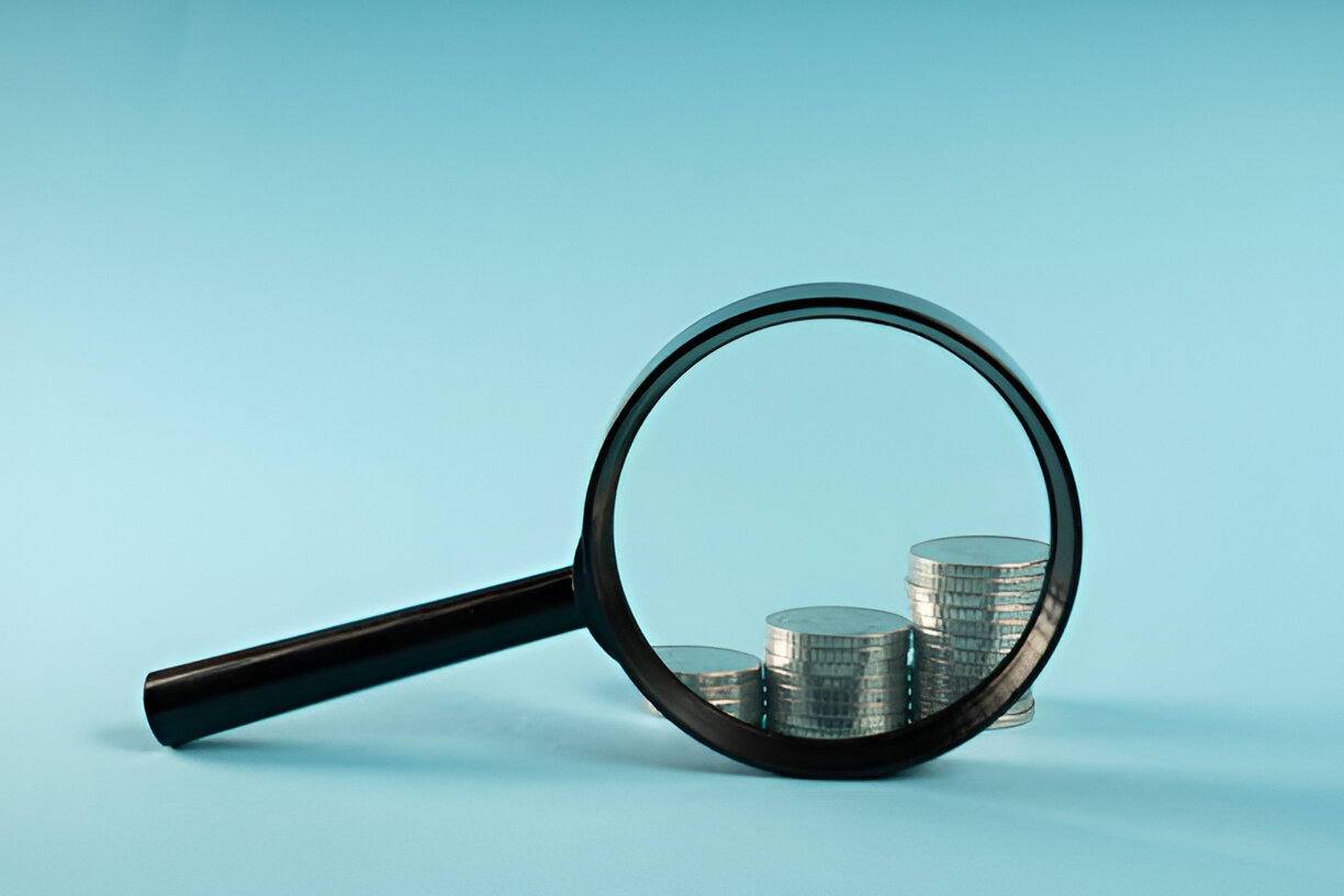  A collection of coins alongside a magnifying glass, set against a blue background, highlighting their intricate details.