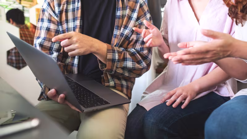 A group of three individuals sitting on a couch, collaborating on a laptop about the 2025 NetSuite Consultant guide.