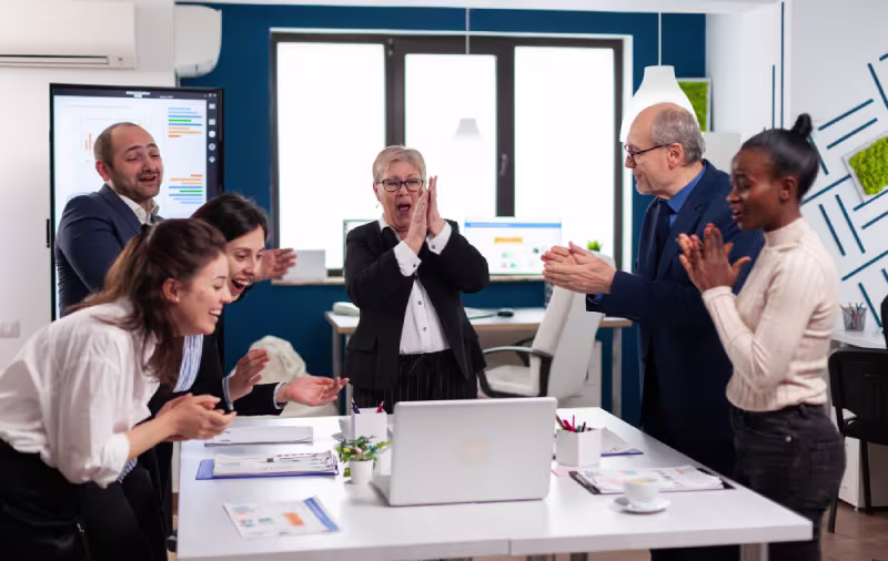 A diverse group of office workers enthusiastically applauding, celebrating a successful presentation on remote ERP accounting solutions.