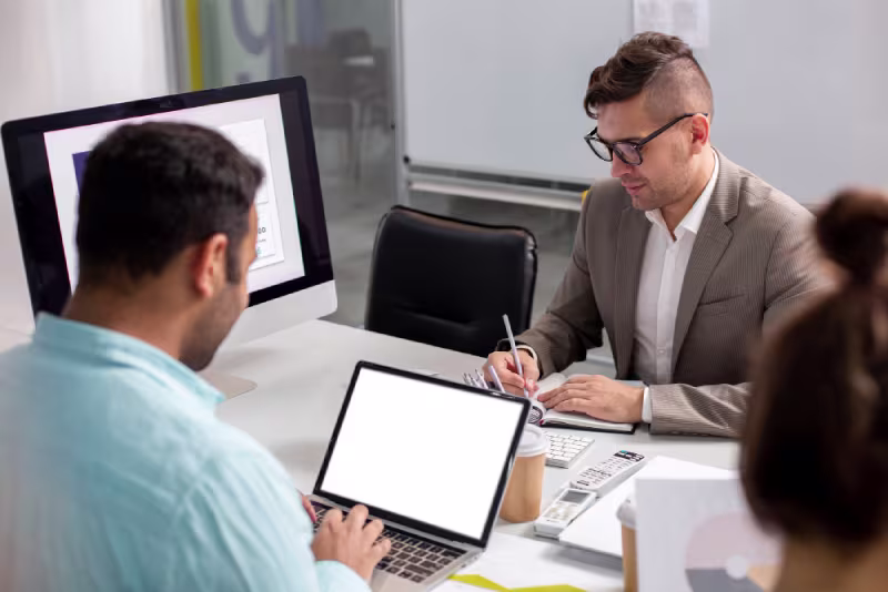 A man and woman sit at a desk with a laptop, discussing the NetSuite Developer interview process and assessment.