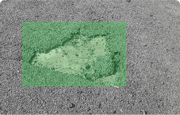 Close-up of damaged asphalt road surface showing a pothole with exposed underlying layer.