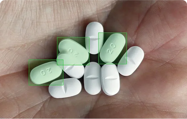 A hand holding eight pills, including three white oblong pills with a score line and three green triangular pills marked with '20'.