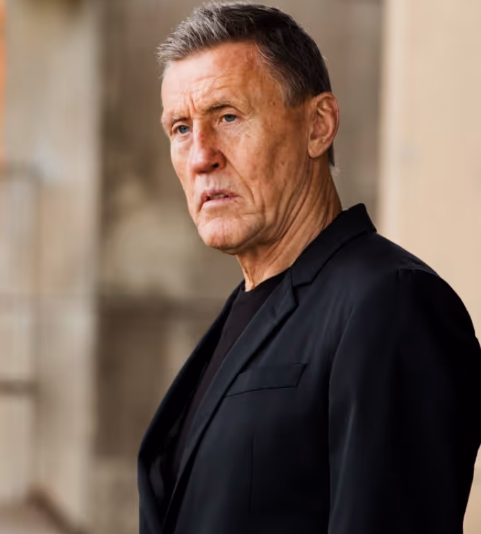 Närbild av en allvarlig äldre man med kort grått hår klädd i svart kavaj.