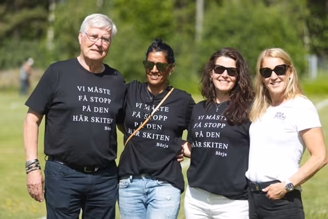 Fyra personer står bredvid varandra på en grön äng. De har svarta t-shirts med texten "Vi måste få stopp på den här skiten".