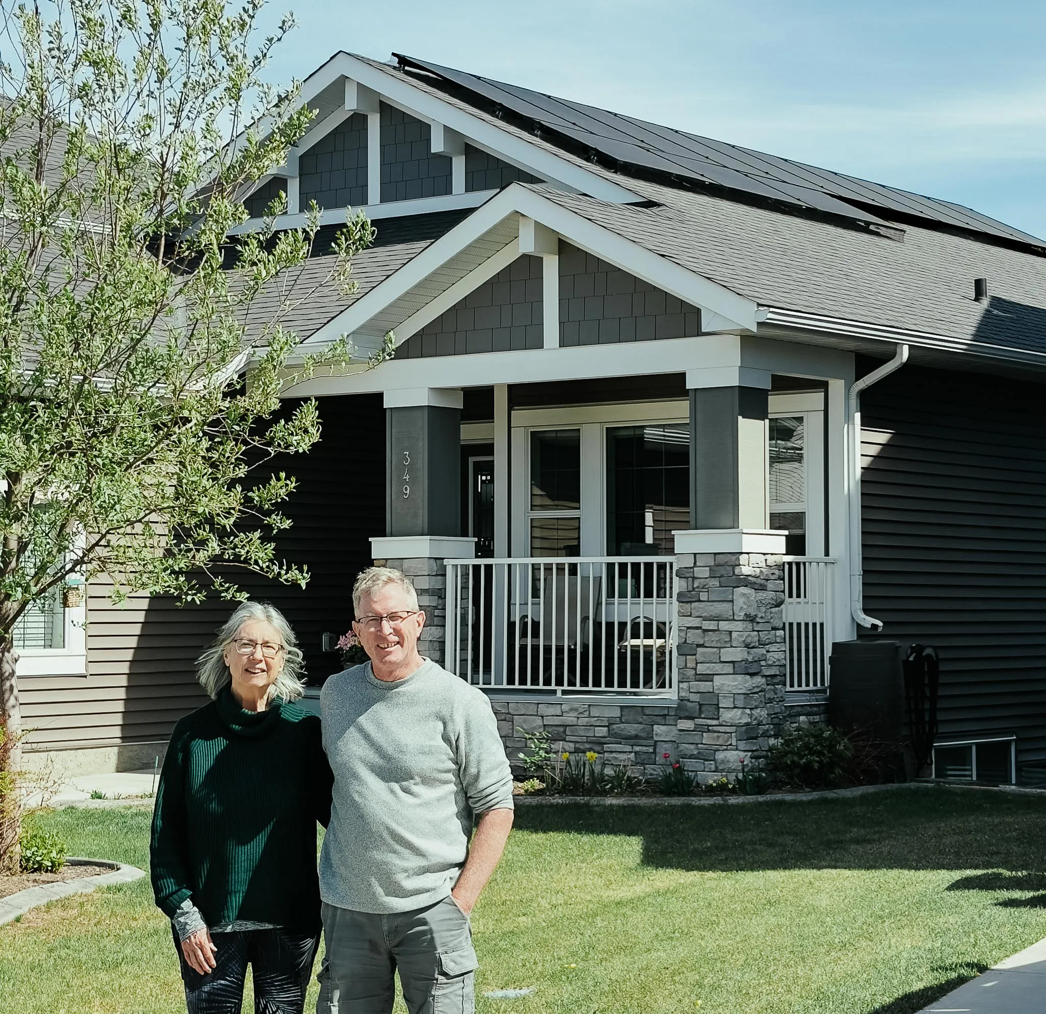 Two Albertan homeowners smiling in front of their new residential solar system installed by Orizon Energy