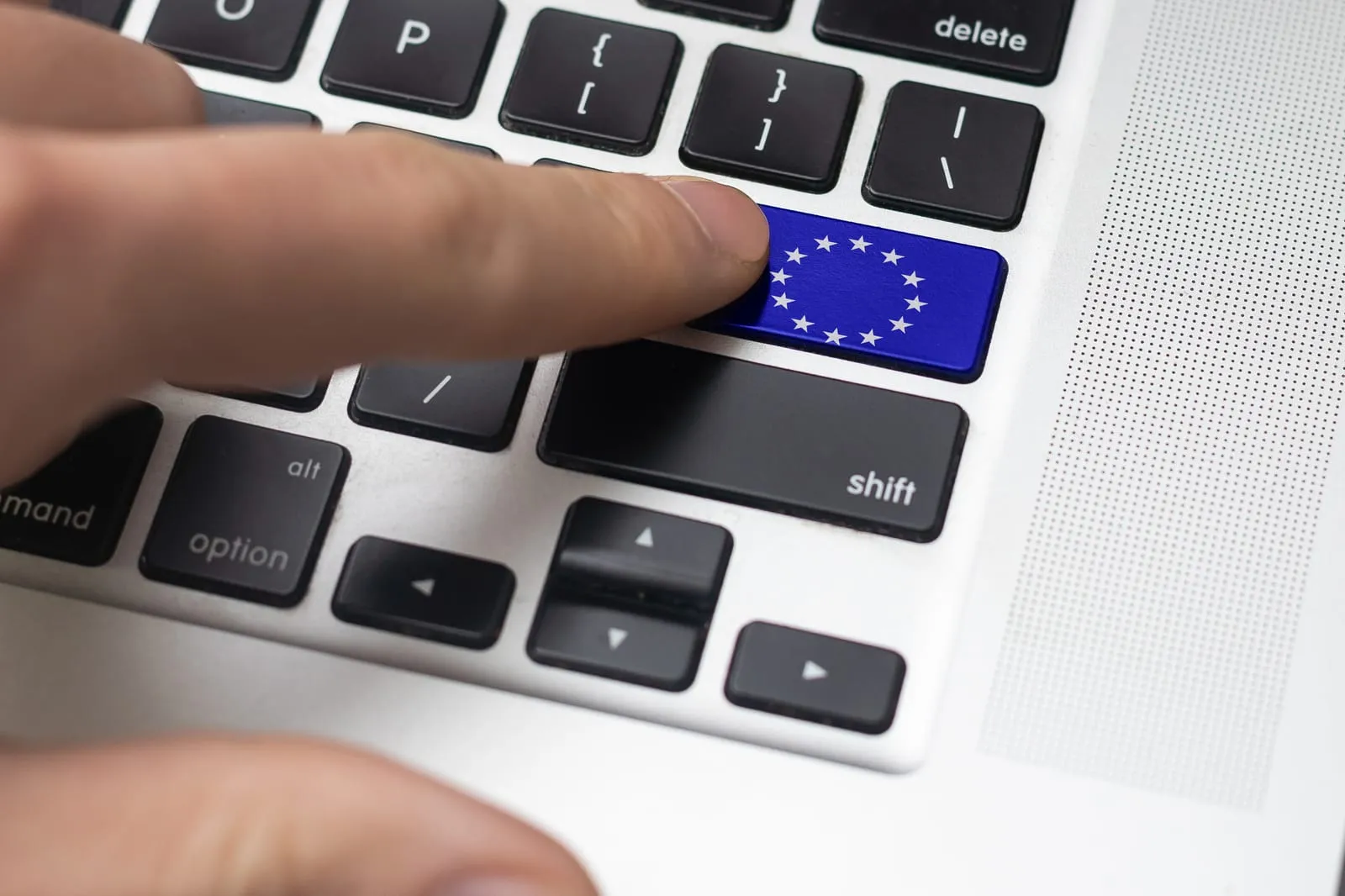 Close-up of a finger pressing a blue keyboard key with the EU flag, representing European Union regulations and digital governance.
