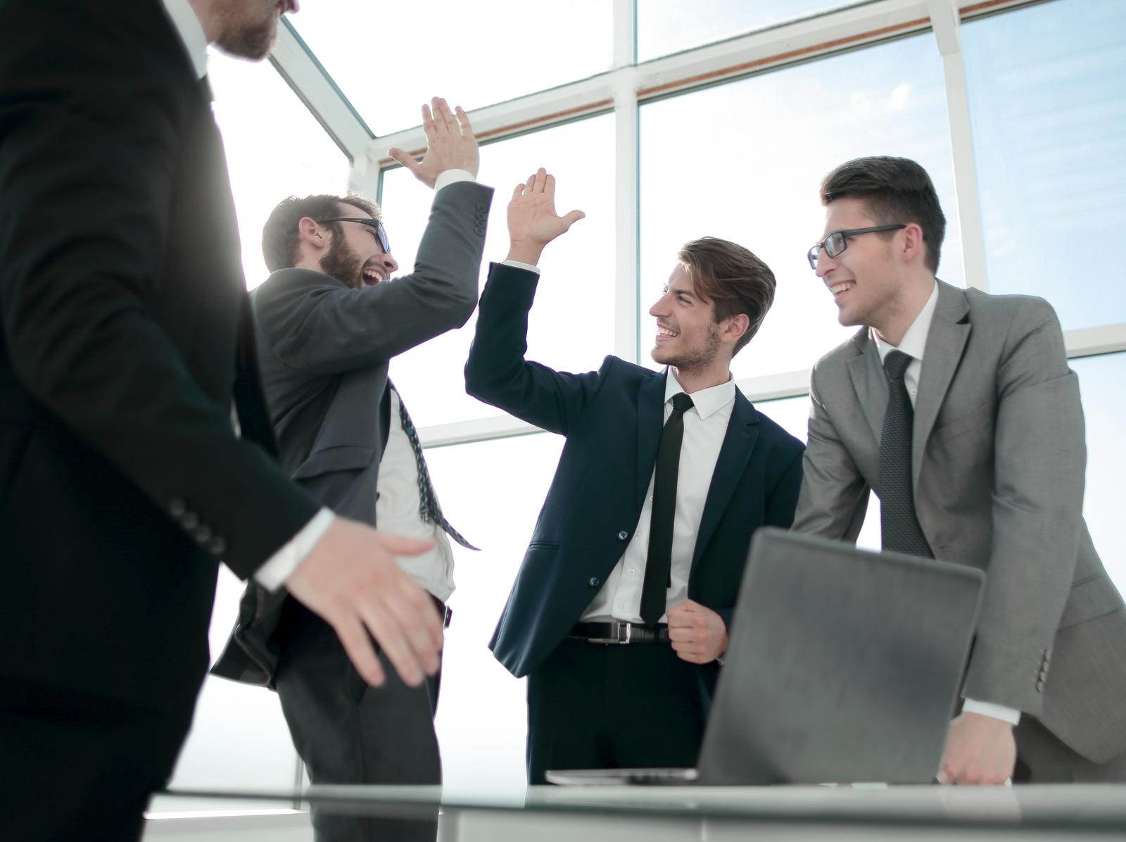 Happy coworkers in business suits giving each other a high-five in a bright modern office, celebrating success