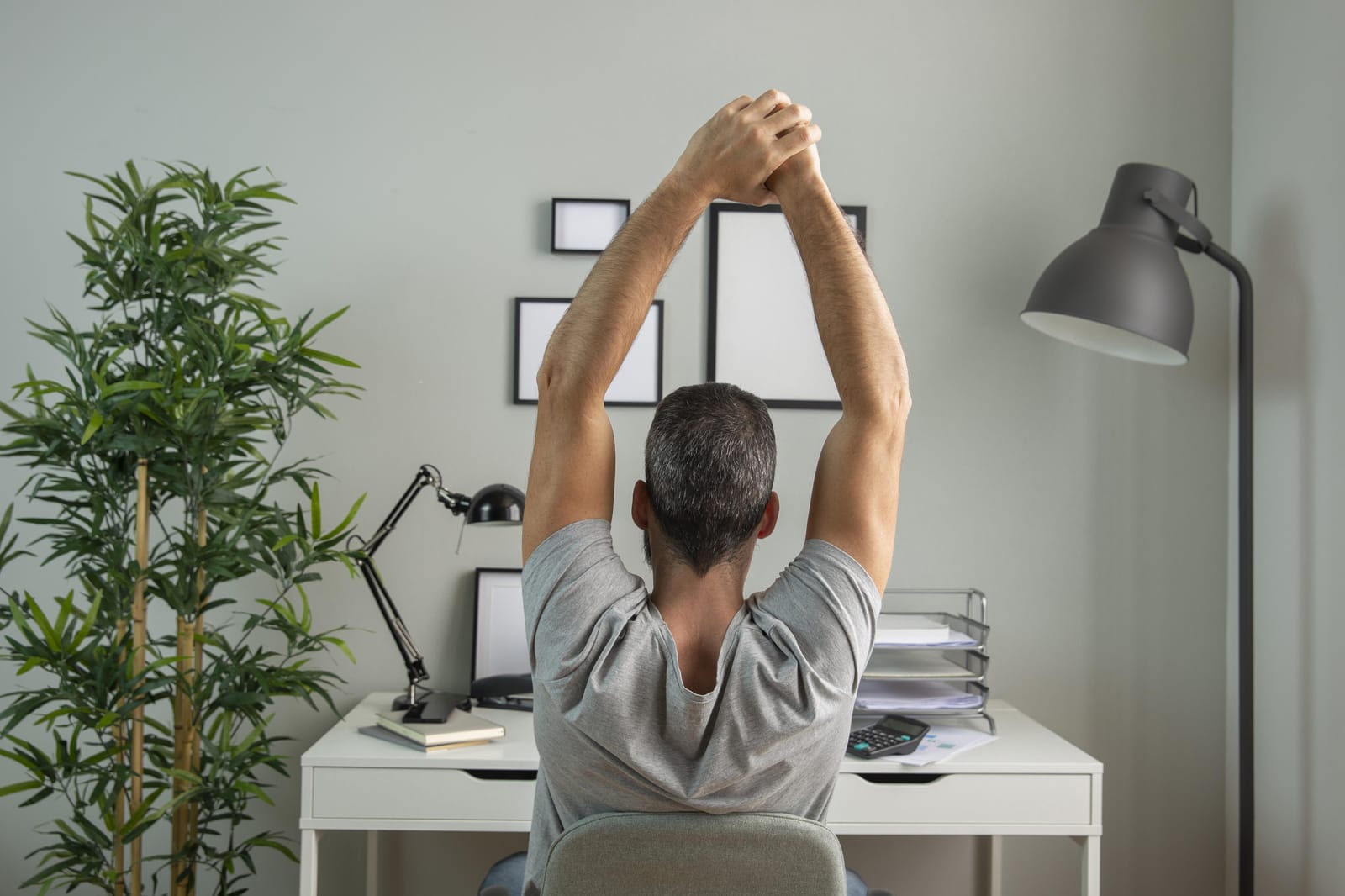 Man stretching his arms overhead while sitting at a desk in a home office, taking a break from work.